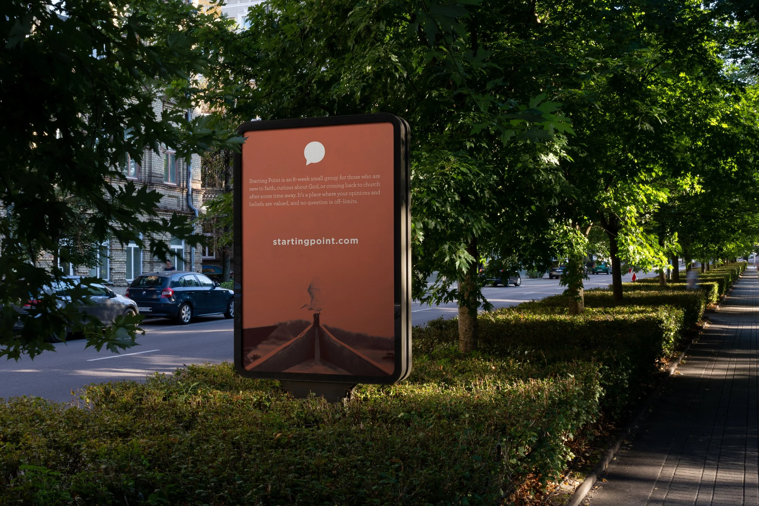Outdoor digital billboard near a sidewalk, trees, and cars, displaying the website startingpoint.com with a background of a boat on water at sunset.