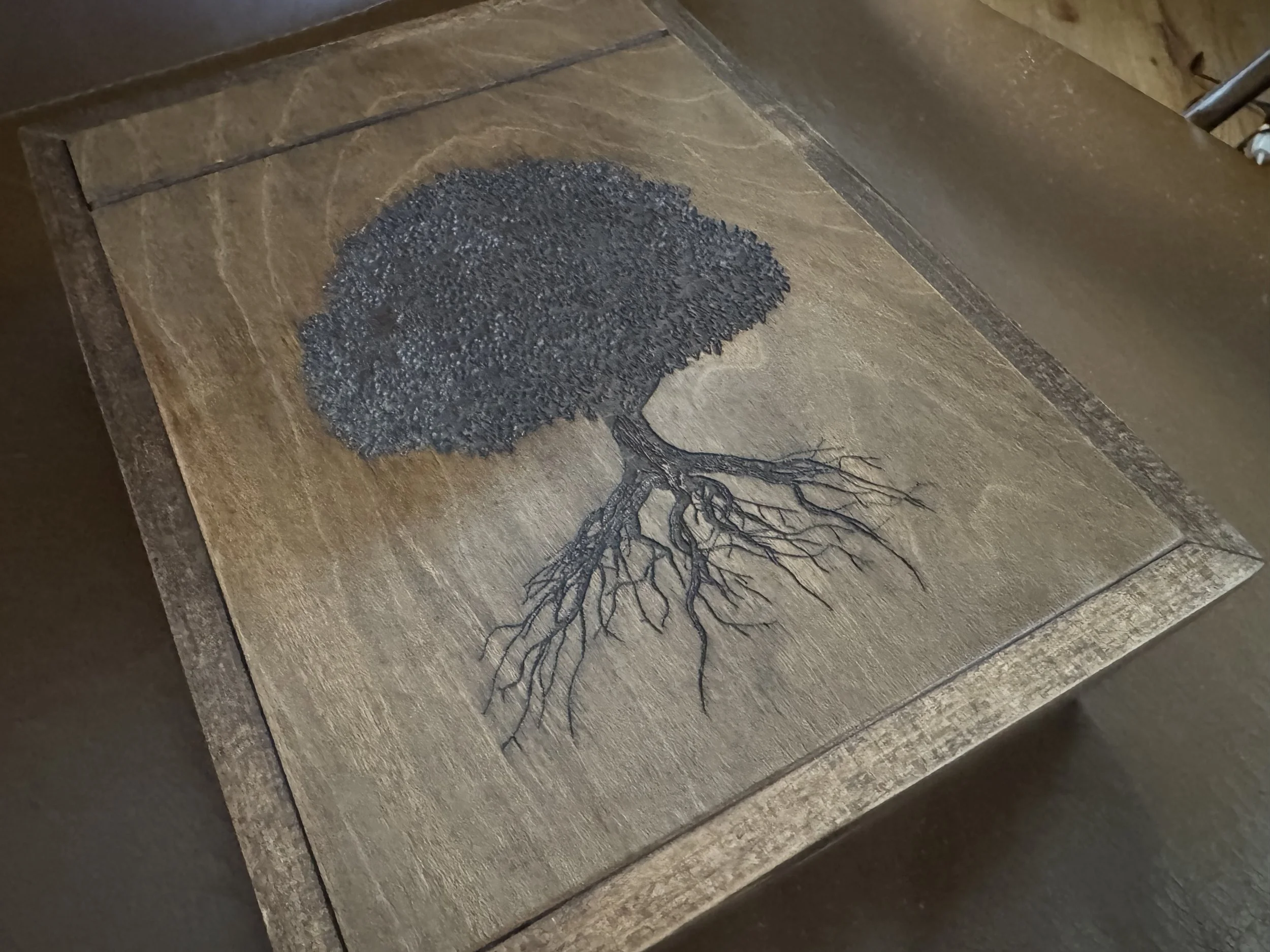 Wooden table with a tree illustration, showing dark green leaves and black branches that extend into roots.