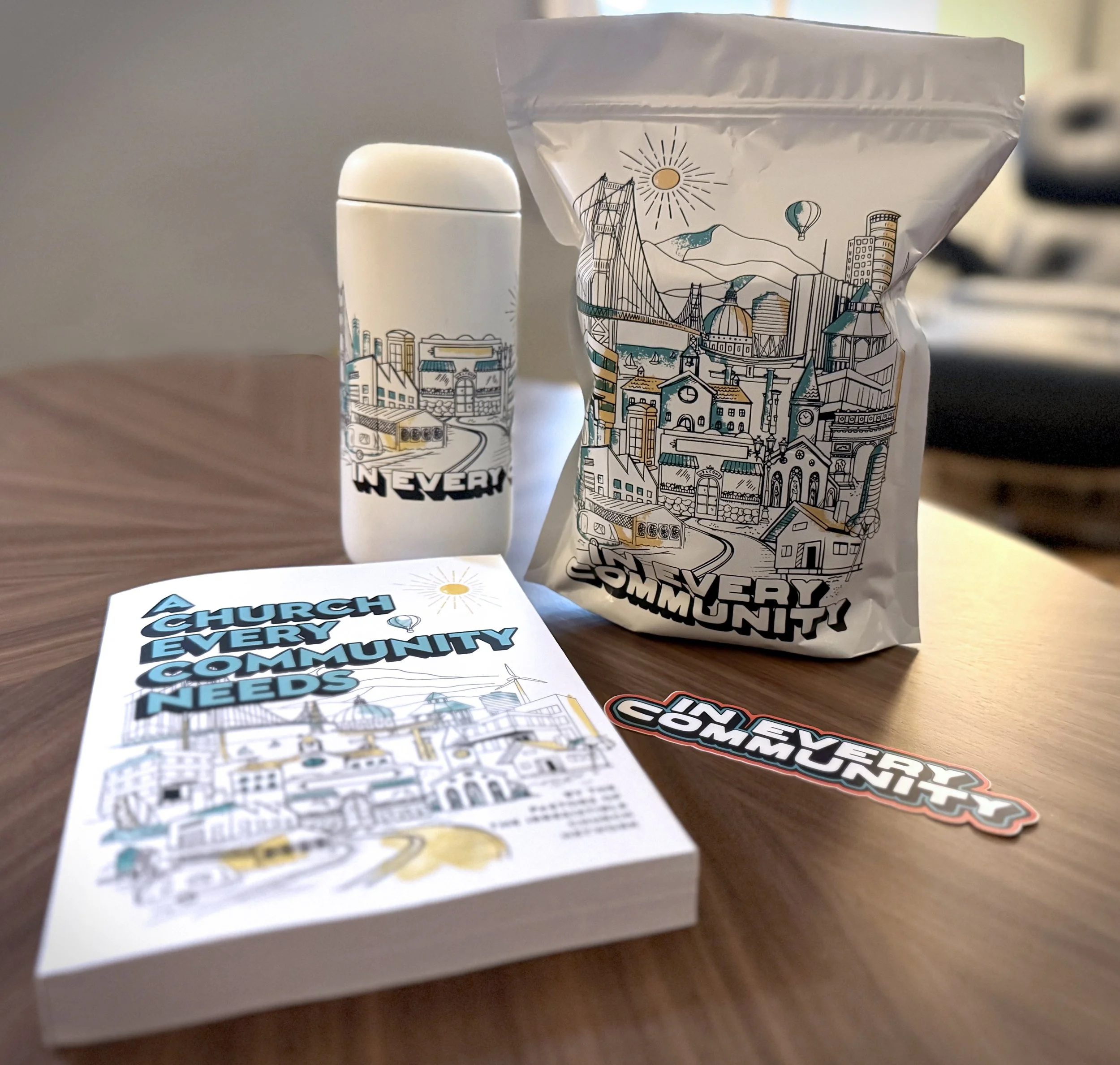 A collection of items featuring a cityscape illustration with buildings, bridges, and a sun. The items include a white thermos, a paper bag, a booklet, and a sticker, all with the same design and the text 'A Church Every Community Needs'.