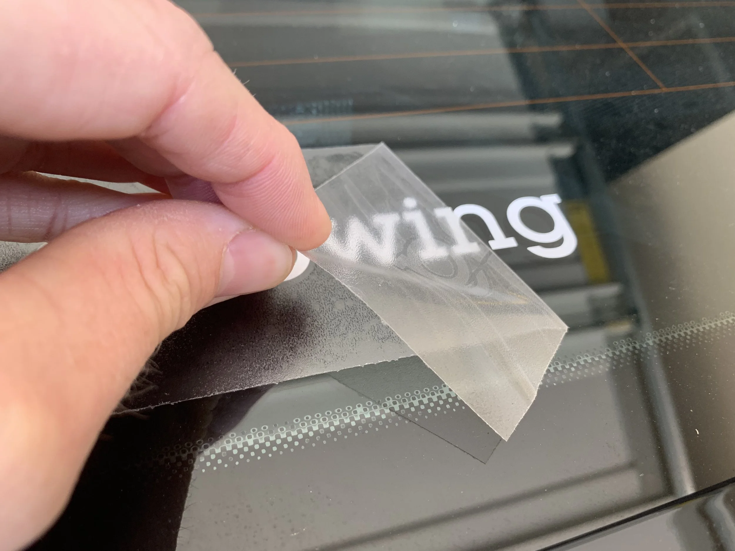 A person peeling a clear adhesive sticker from a sheet on a glass window or door.