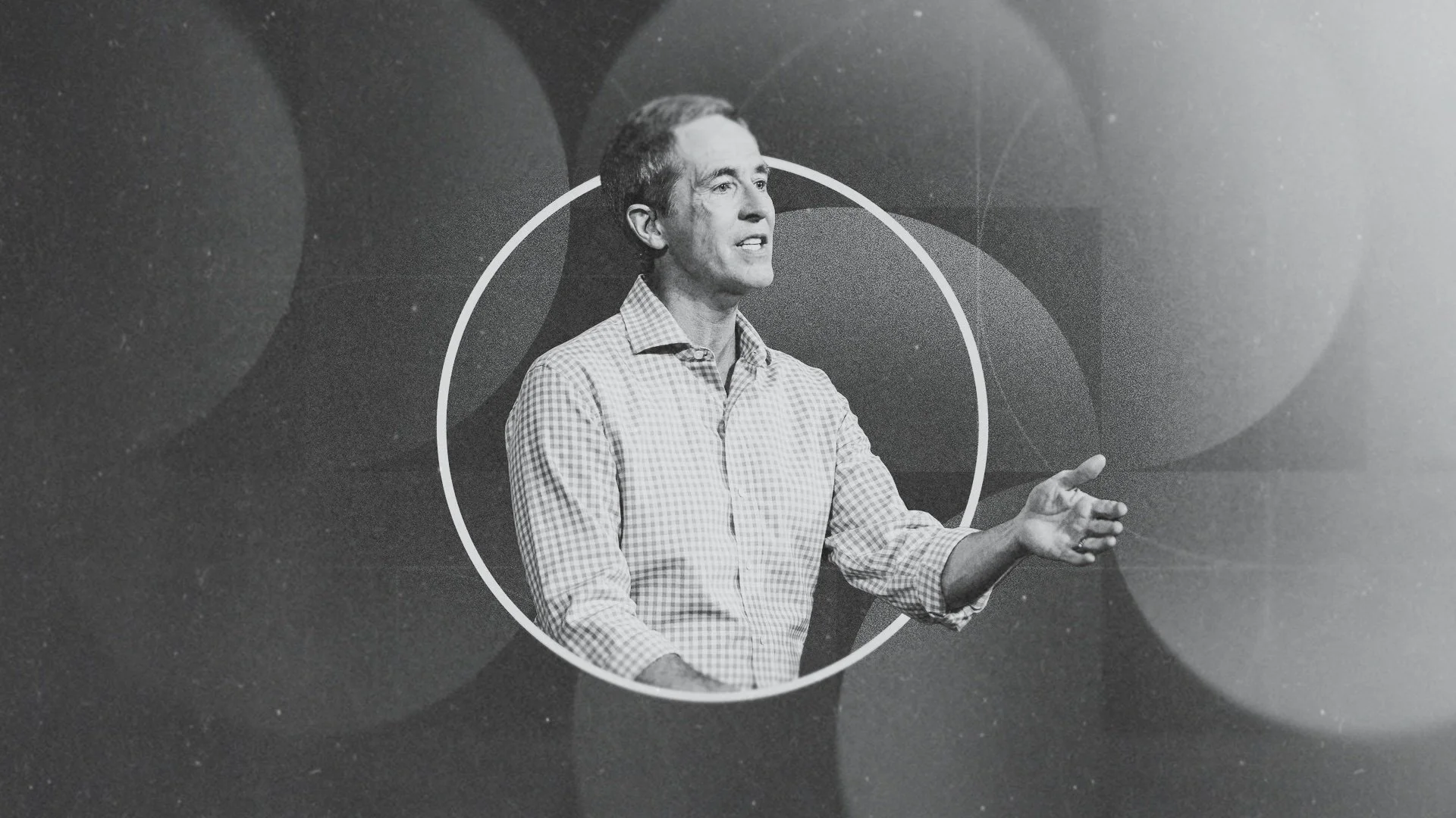 Black and white photo of a man giving a speech or presentation, gesturing with his right hand, standing within a white circular outline on a dark background with large, overlapping circles.