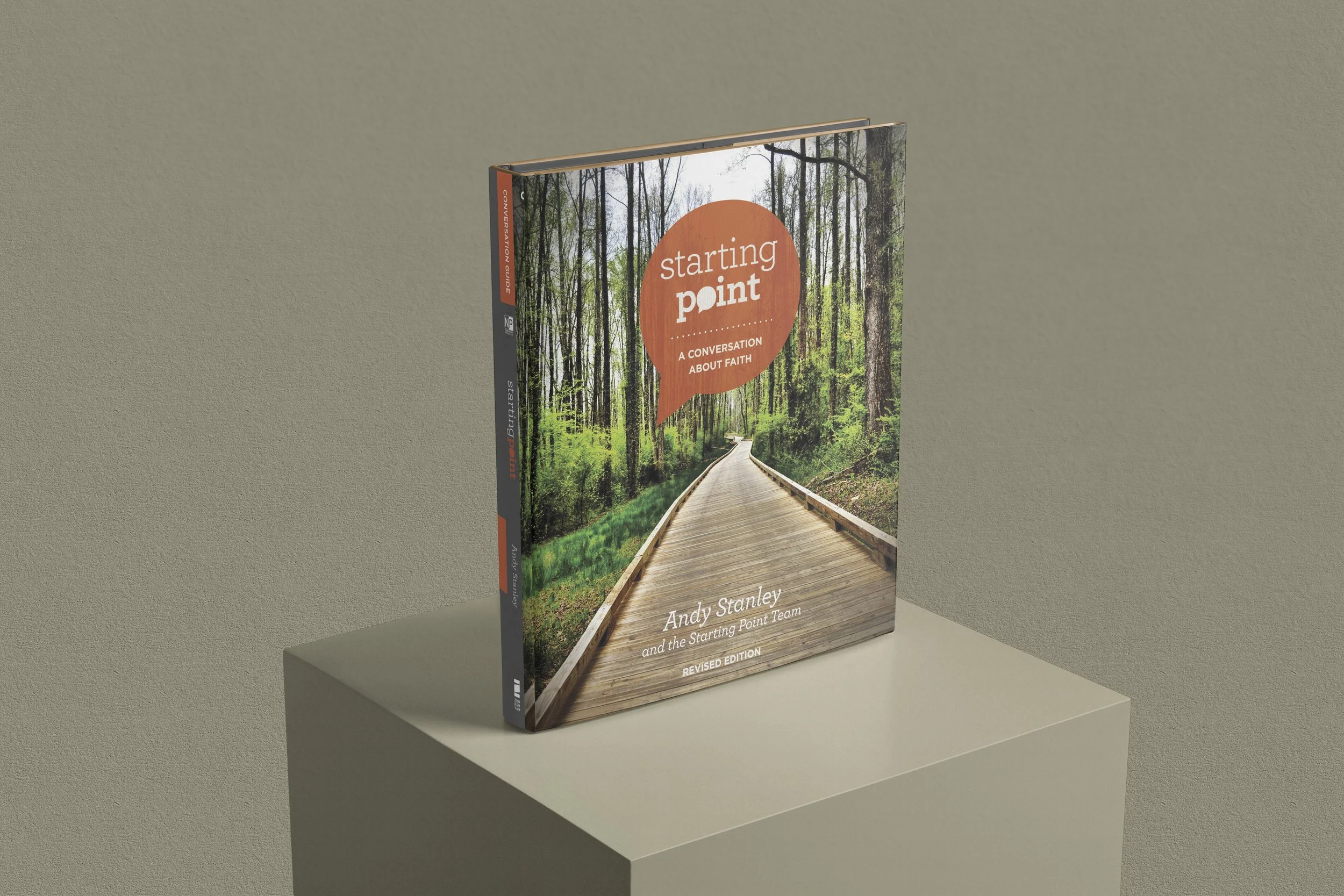 Book titled 'Starting Point: A Conversation About Faith' by Andy Stanley on a white pedestal, featuring a cover with a forest and wooden pathway.