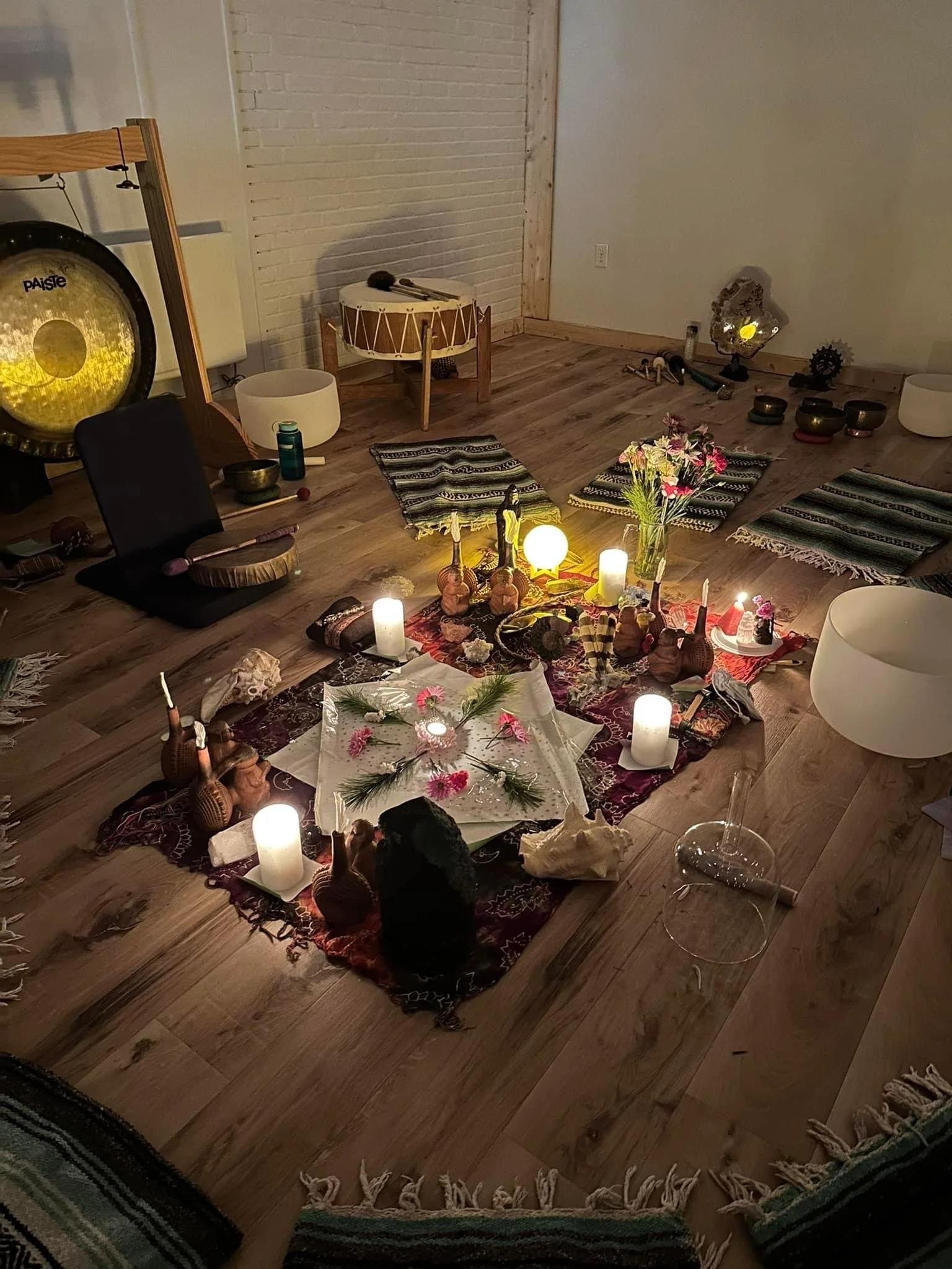 Decorative altar with candles, flowers, figurines, and musical instruments in a cozy indoor space with wooden floors and woven rugs.