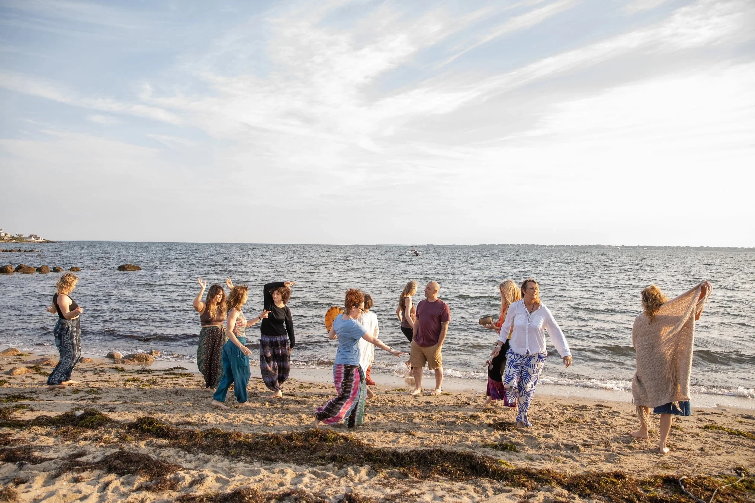 Group of people dancing along a sandy beach in Fairhaven near the ocean during sunset.