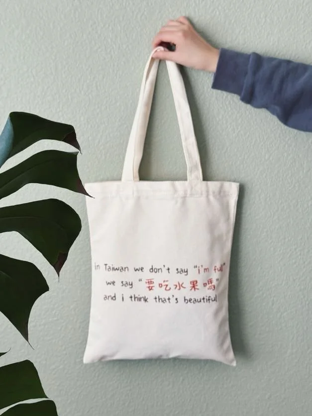 Back of canvas tote bag with the phrase “In Taiwan, we don’t say I’m full, we say would you like some fruit” printed in text.