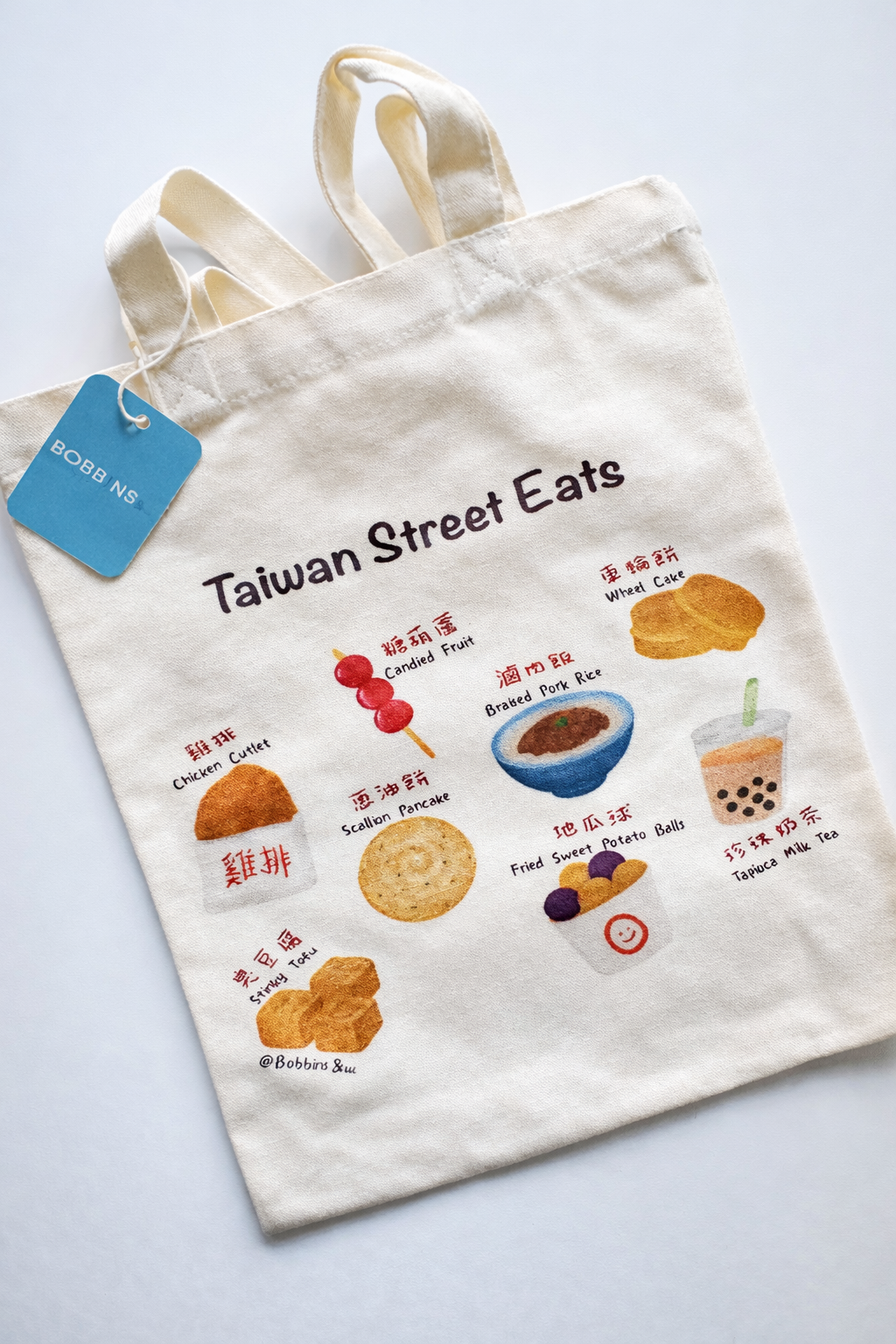 Close-up of Taiwan Street Eats tote bag with illustrated dishes and blue bobbins& tag in the top left corner.