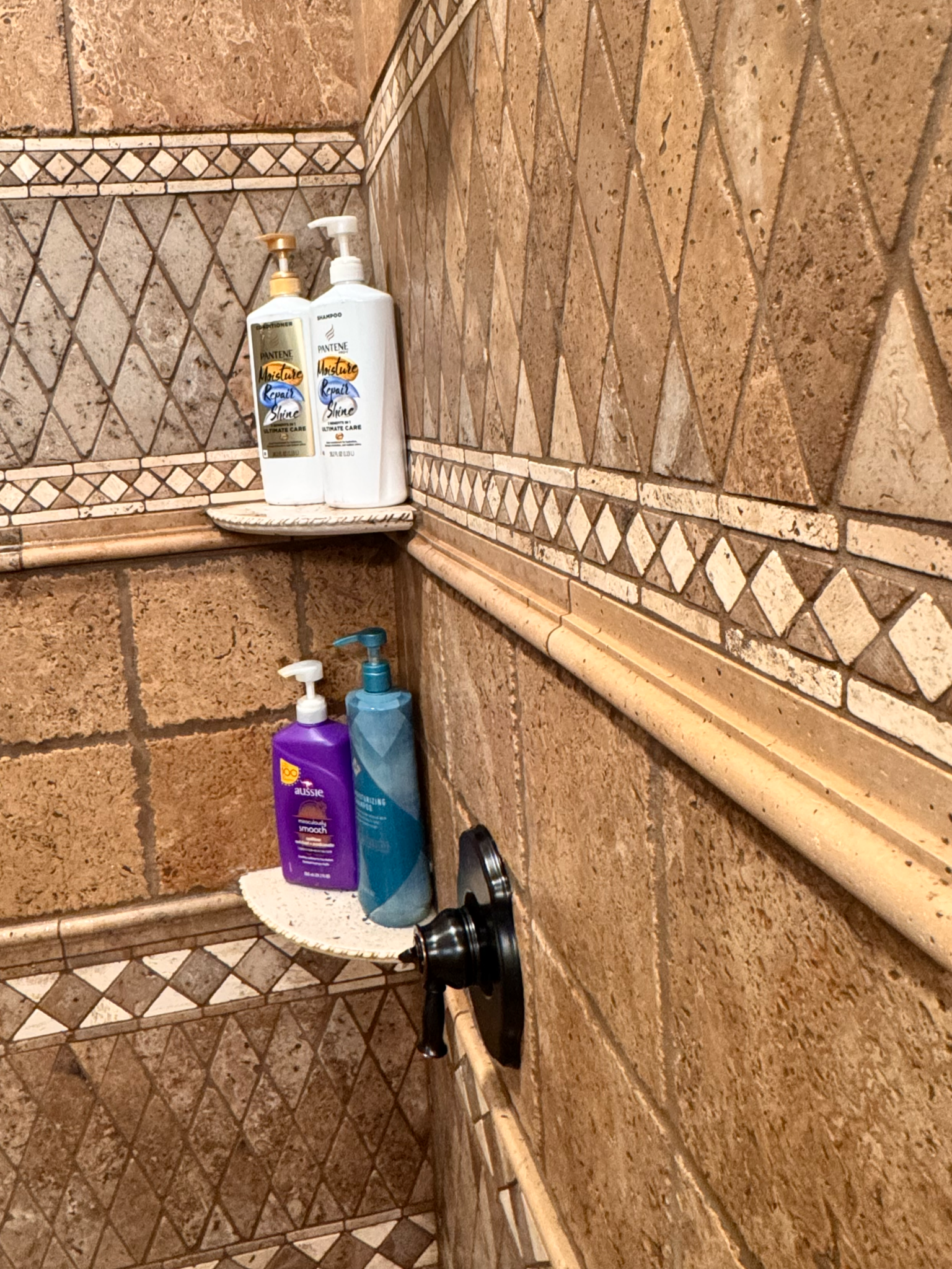 Bathroom shower corner with bottles of body wash, shampoo, and conditioner on a small shelf.