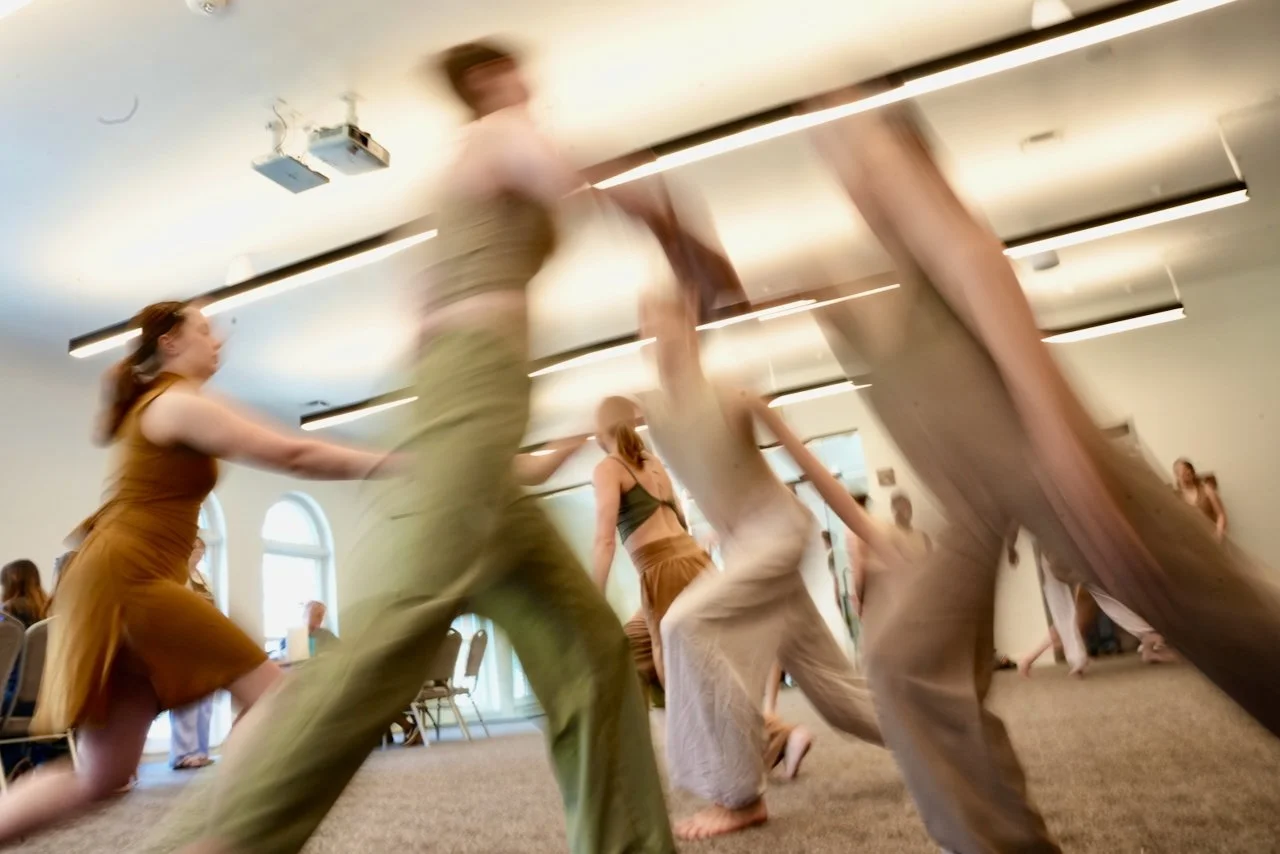People dancing in a spacious room with high ceilings, large arched windows, and modern lighting.