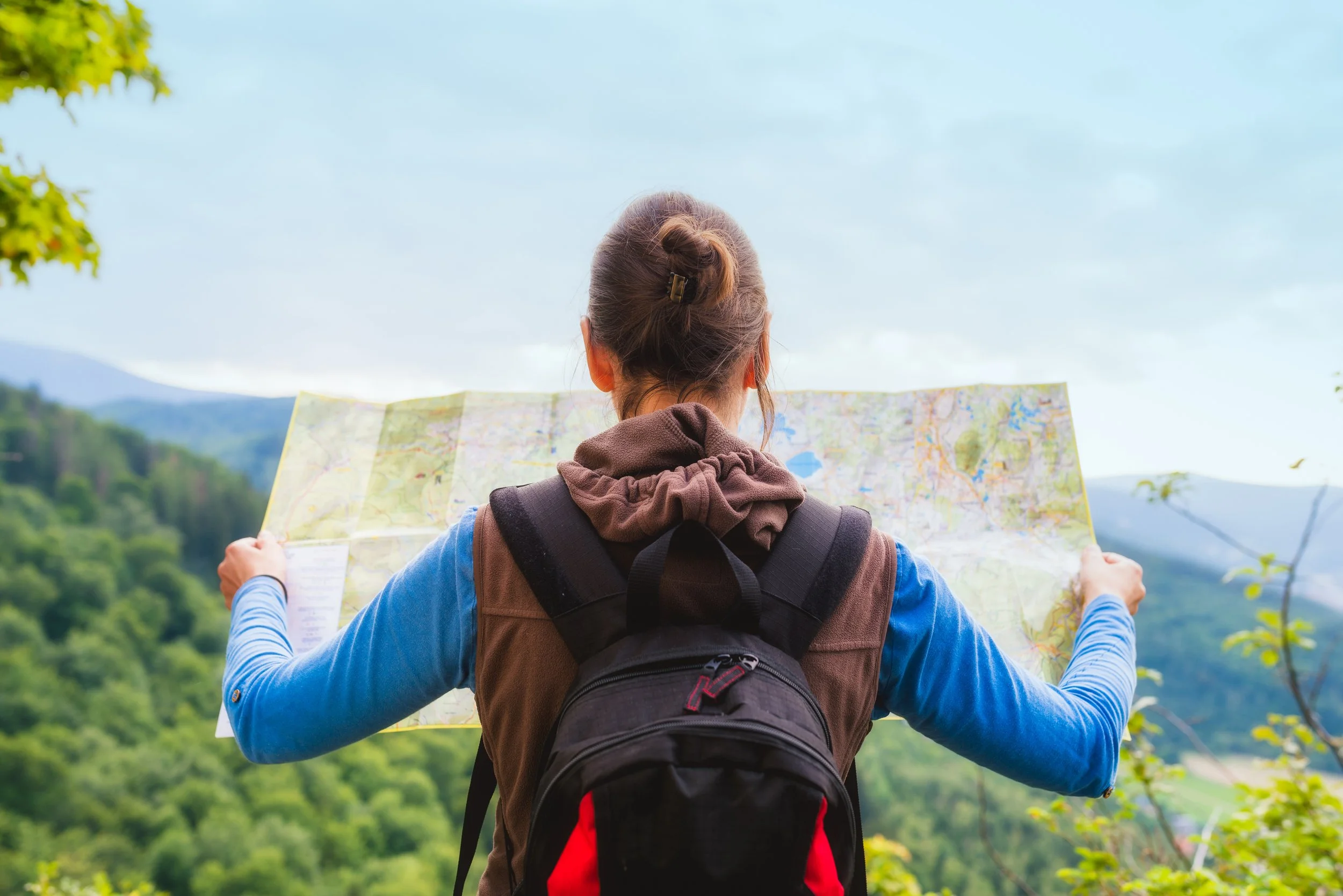 A woman with a backpack holds a map and looks at the mountain scenery.