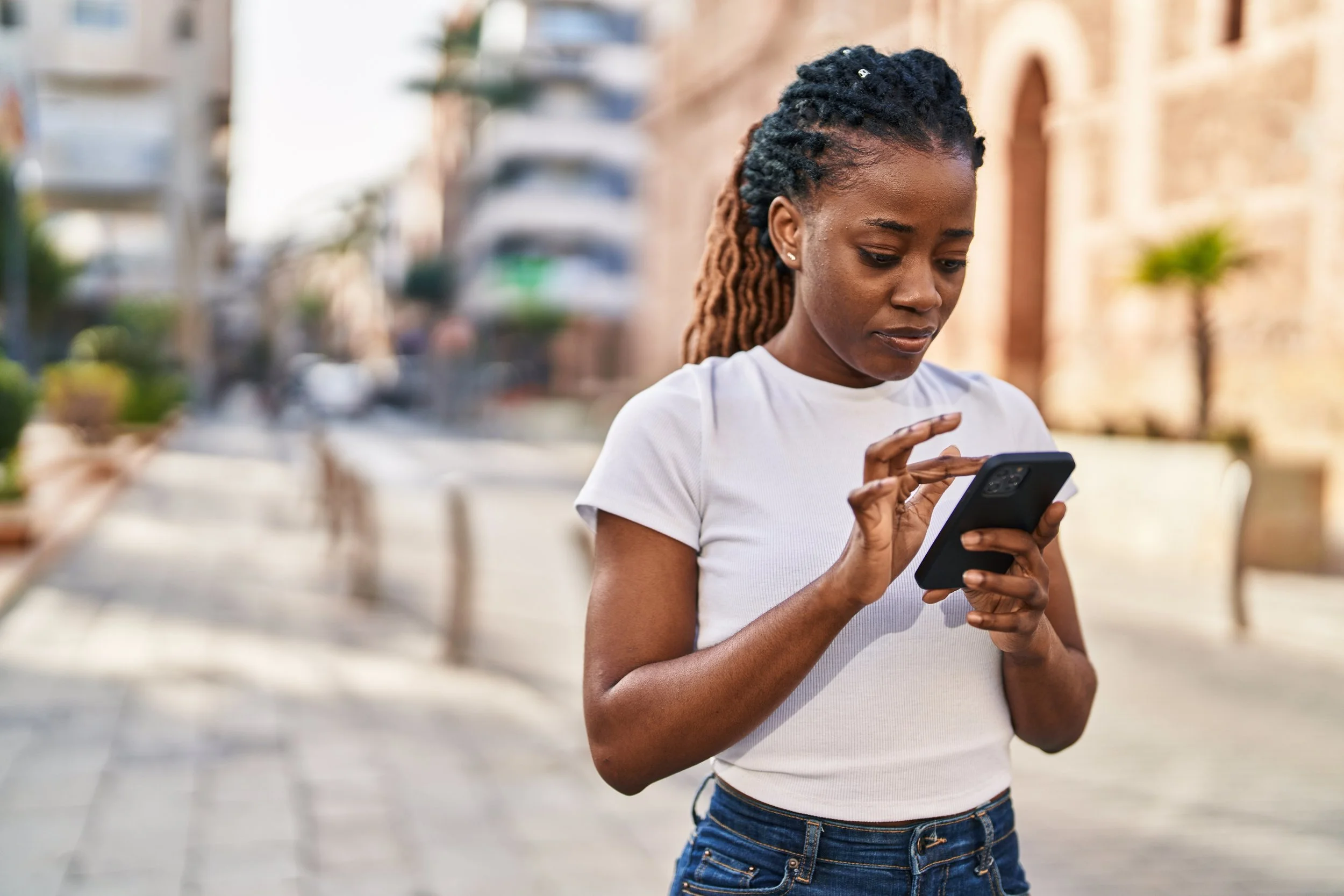 Young woman standing outside and typing on her phone with a serious expression.