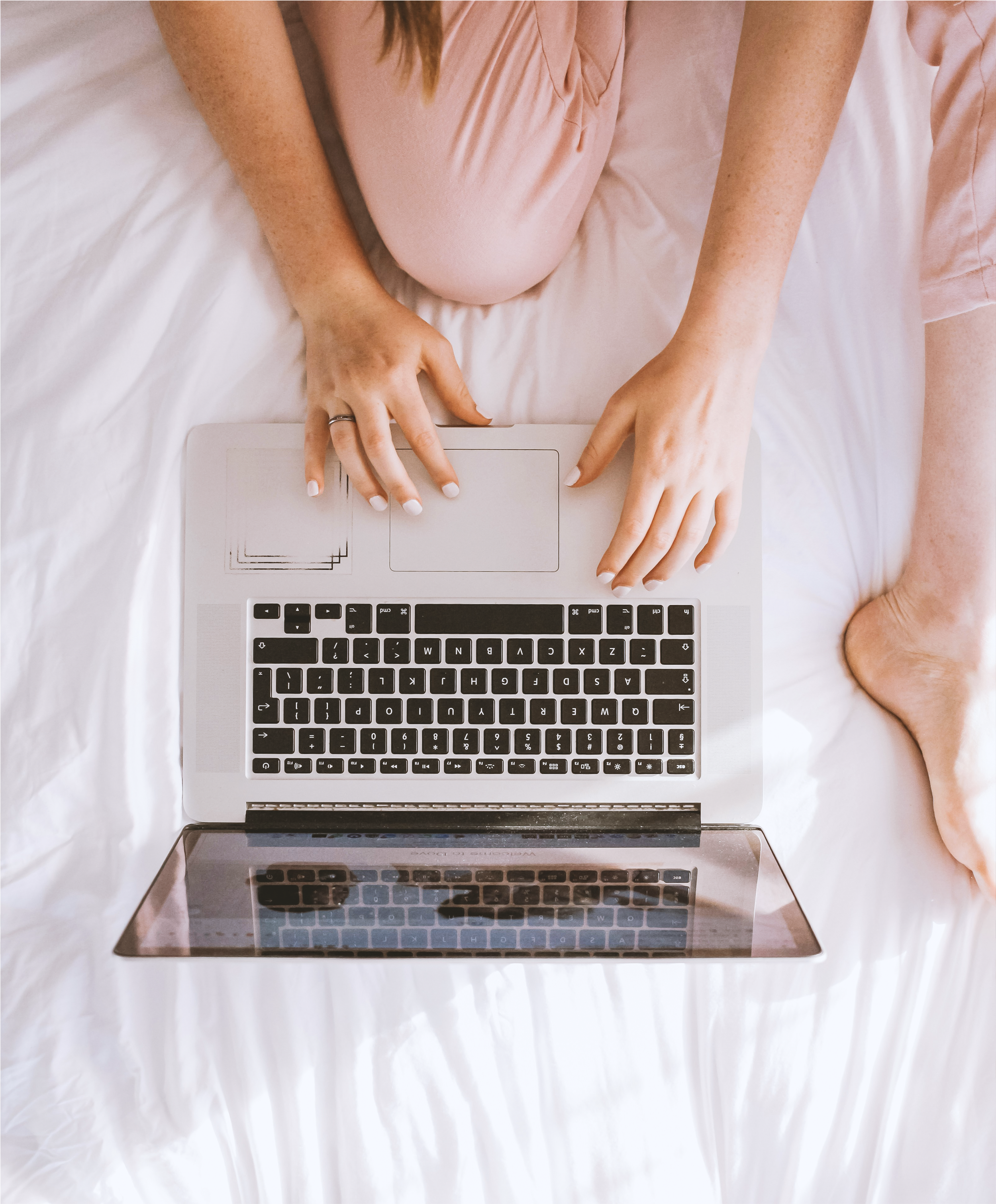 Woman typing on her laptop while sitting on her bed.