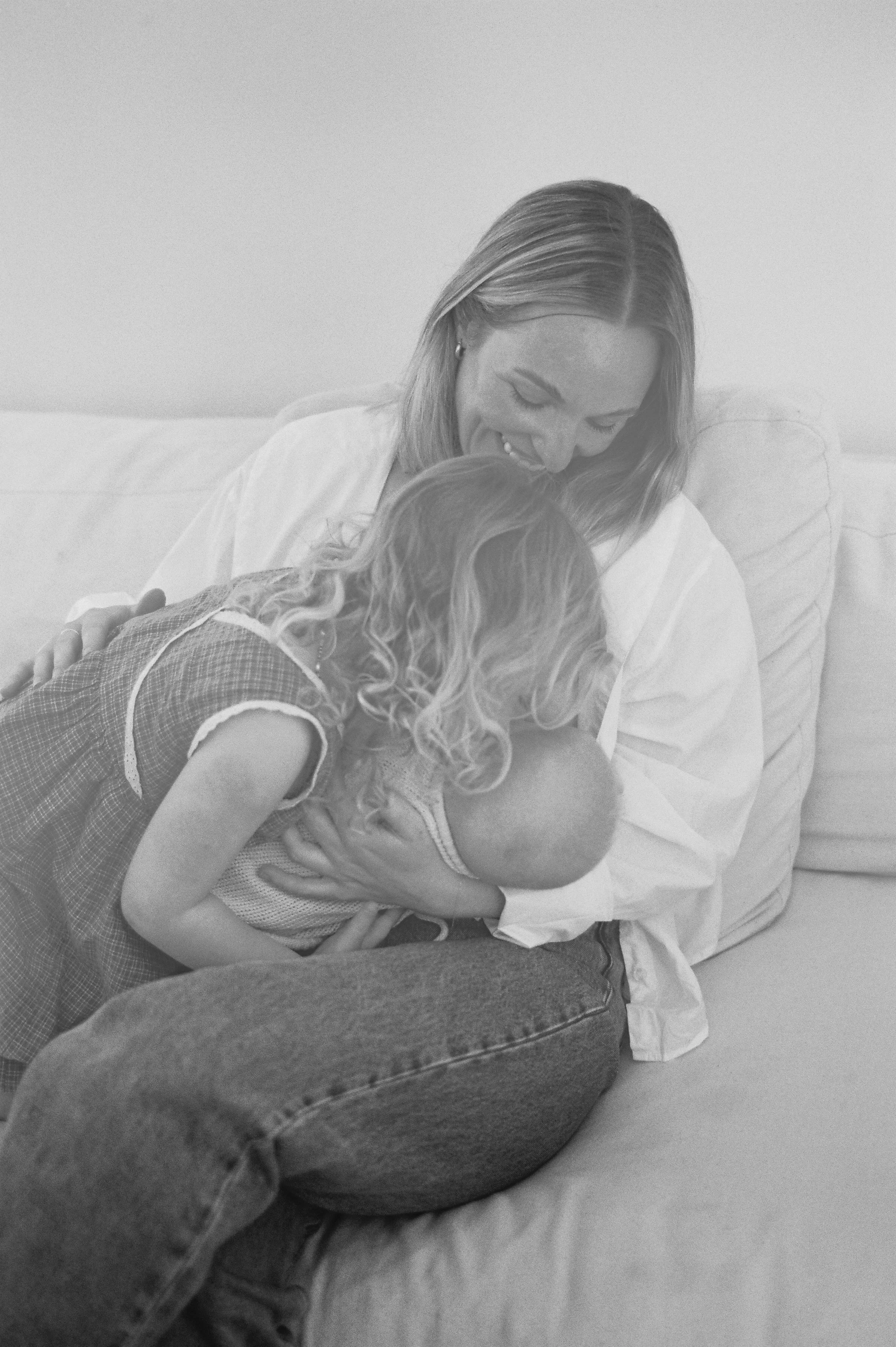 A woman holding a young girl and a baby on her lap, sitting on a couch, sharing a joyful moment.