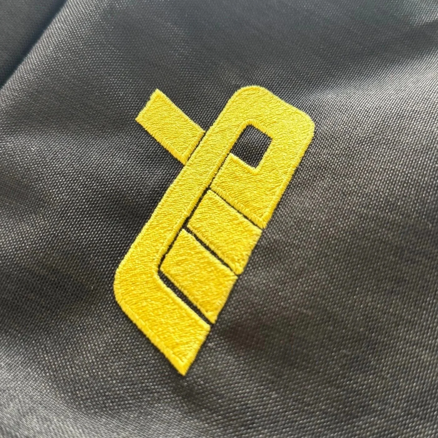 Close-up of a yellow embroidered logo on black fabric.