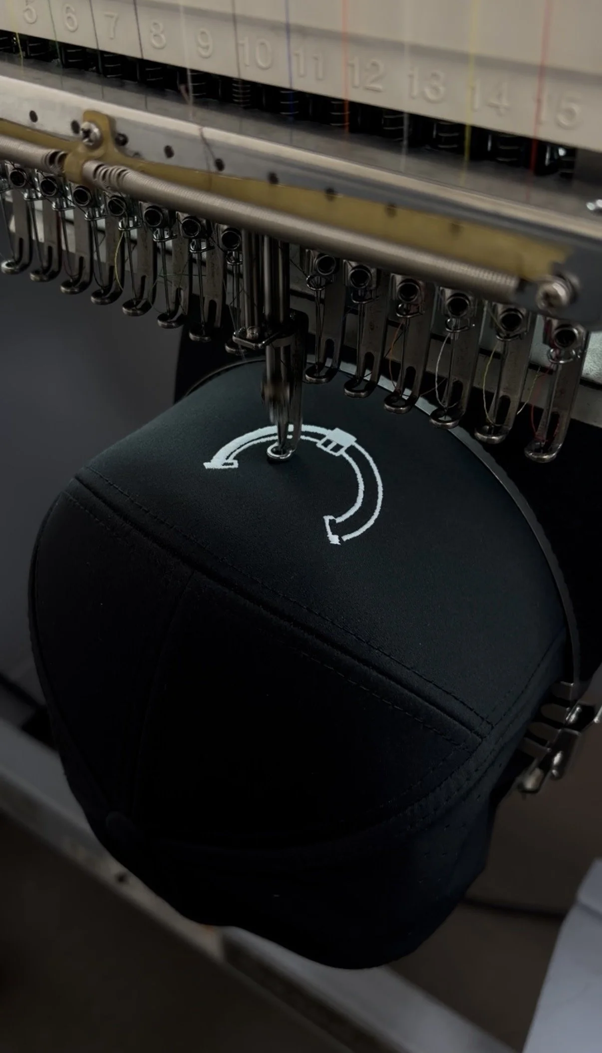 Close-up of a sewing machine embroidery module stitching a white circular design on black fabric.