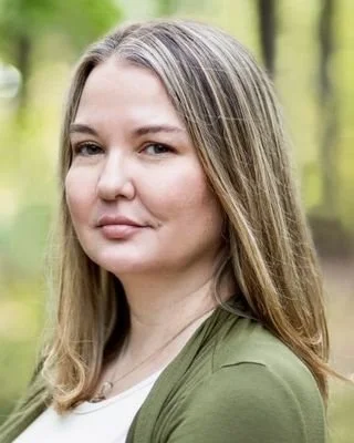 A portrait of an Oklahoma therapist with brown hair and smiling warmly before a therapy session.