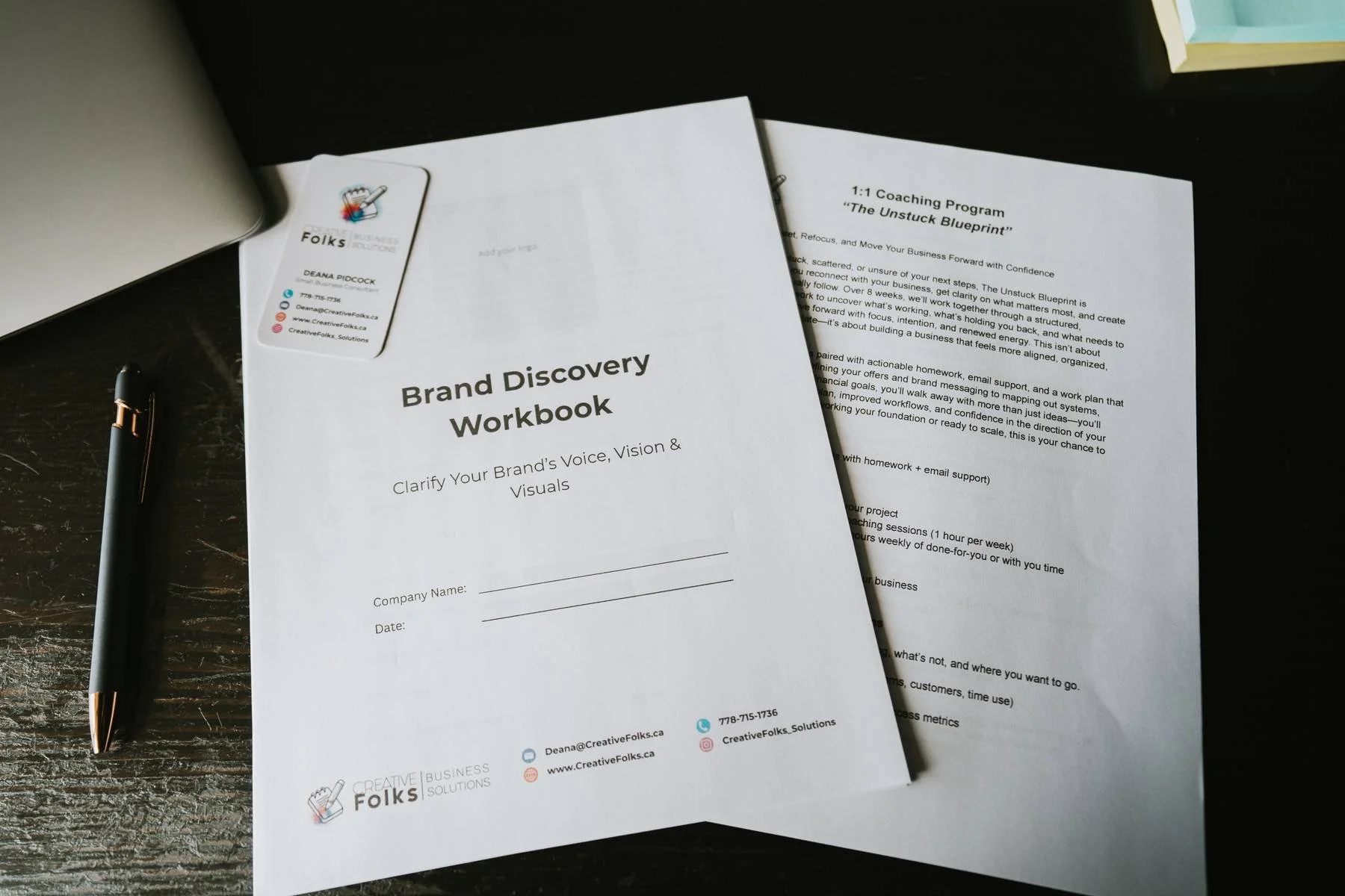 Brand Discovery Workbook titled 'Clarify Your Brand's Voice, Vision & Visuals' on a black desk with a pen beside it, and a second sheet of paper partially underneath.