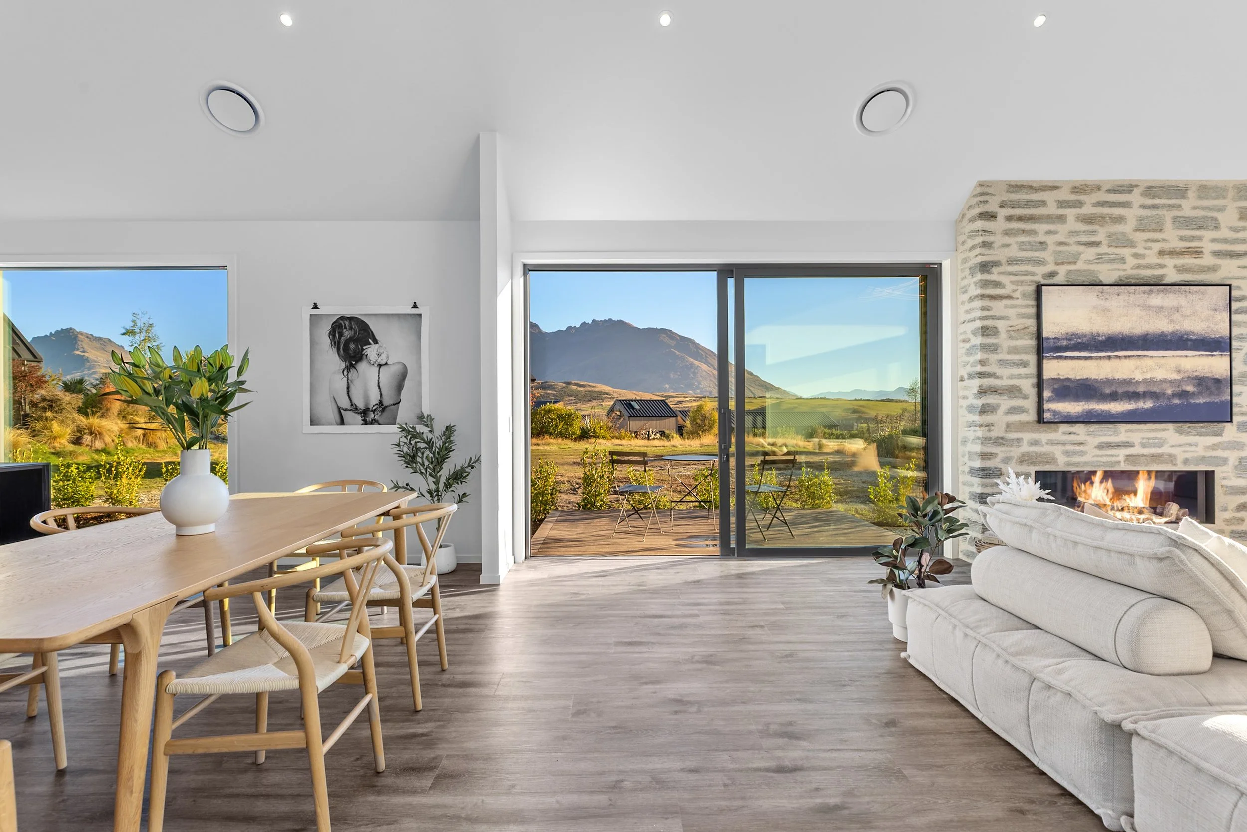 New build living room with stone fireplace, white sofa, and sliding doors to deck with mountain views — Jacks Point, Queenstown