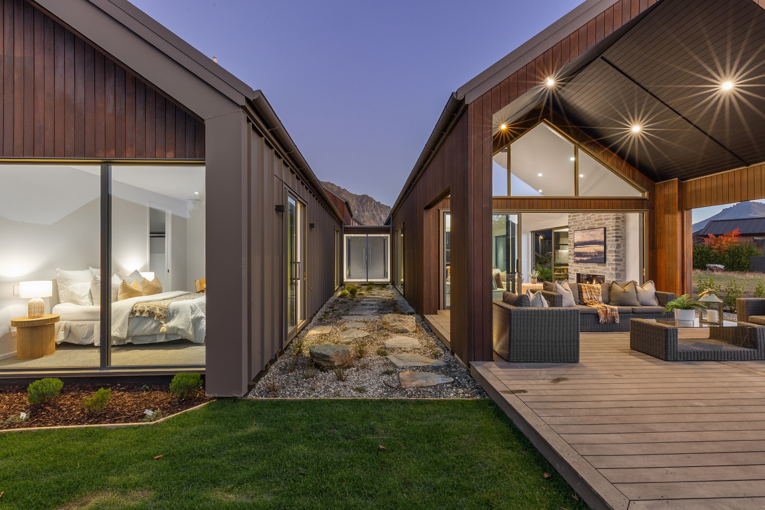 New build exterior at night with stone and timber cladding, interior lighting visible through glass — Jacks Point, Queenstown