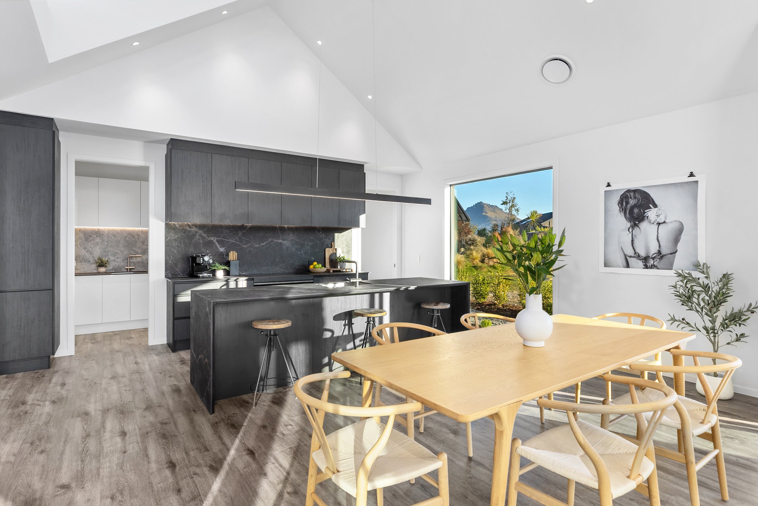 New build kitchen and dining area with wooden table, black island, and exterior views — Jacks Point, Queenstown