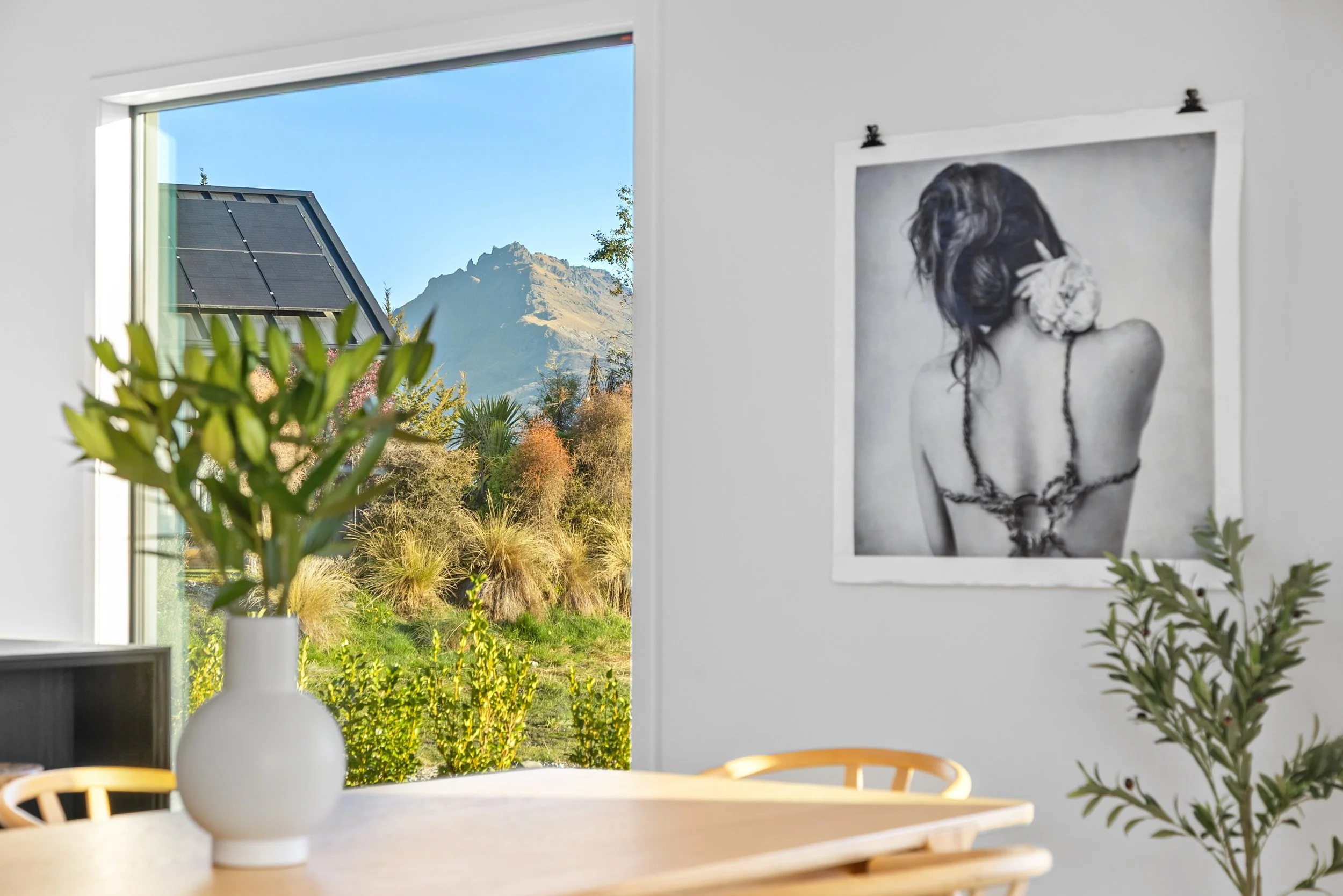 New build interior with mountain view window, black and white art print, and wooden table with plants — Jacks Point, Queenstown