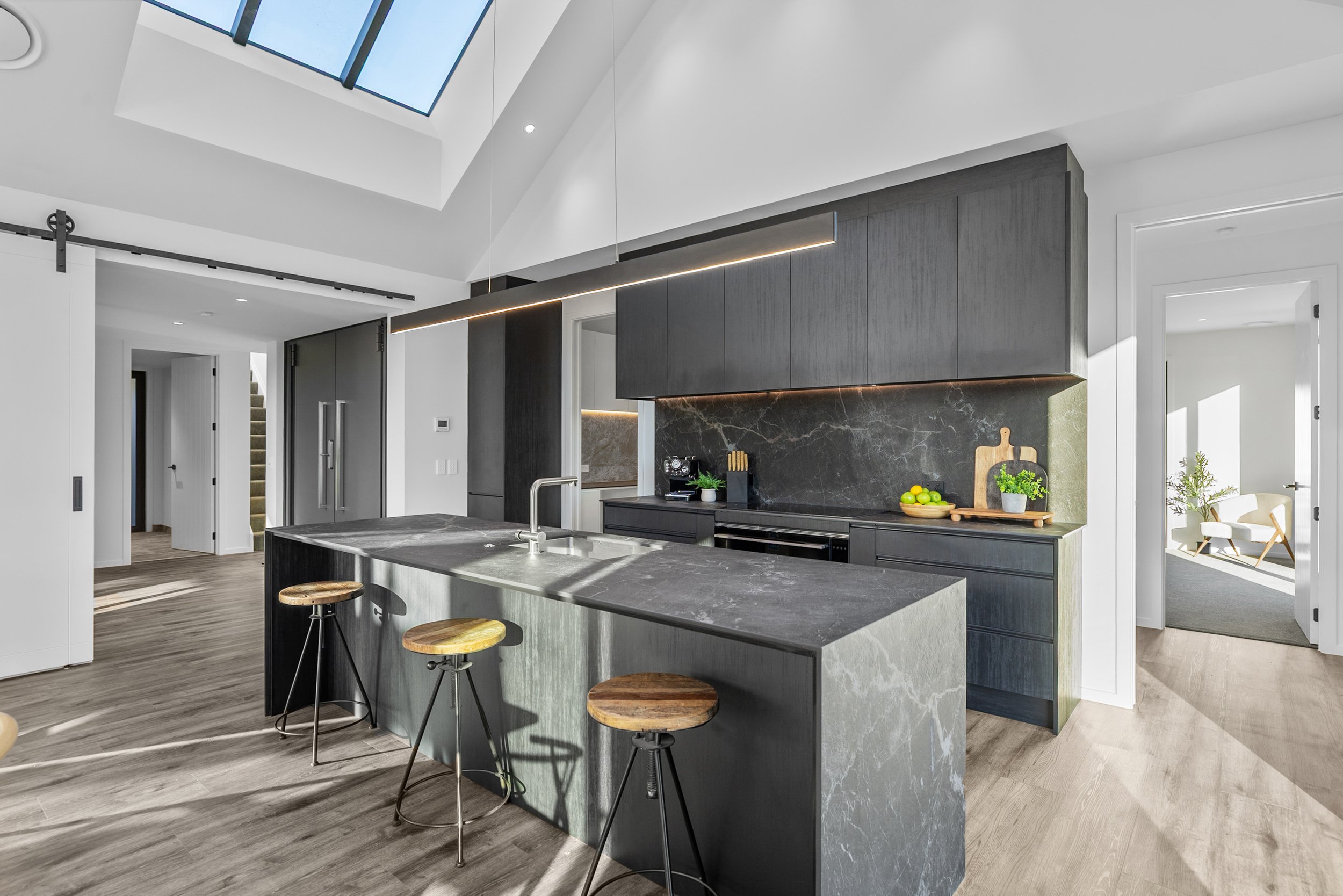New build kitchen with dark cabinetry and marble countertop, opening to bright sitting area — Jacks Point, Queenstown