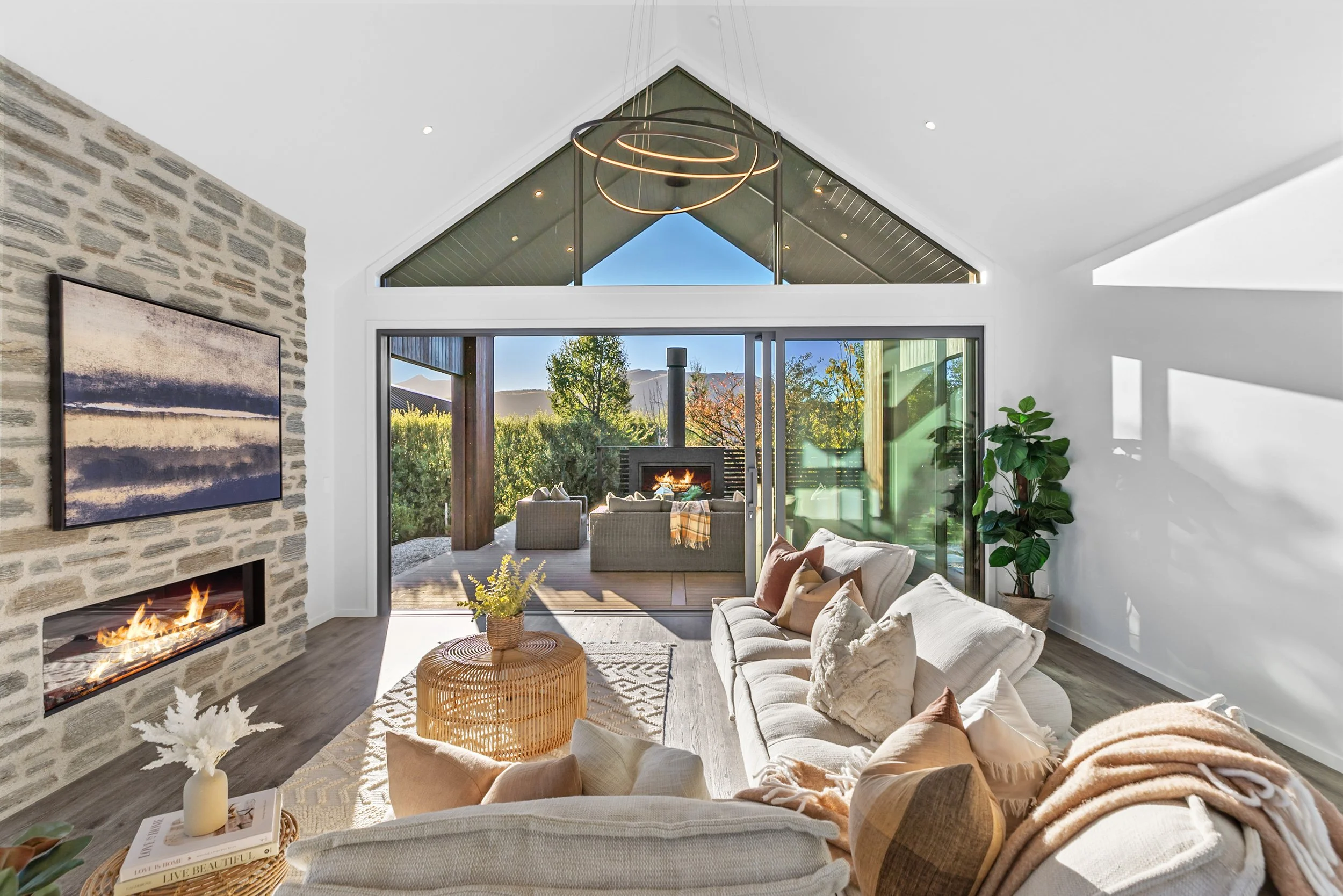 New build living room with stone accent wall, fireplace, and sliding doors to outdoor patio and mountain views — Jacks Point, Queenstown