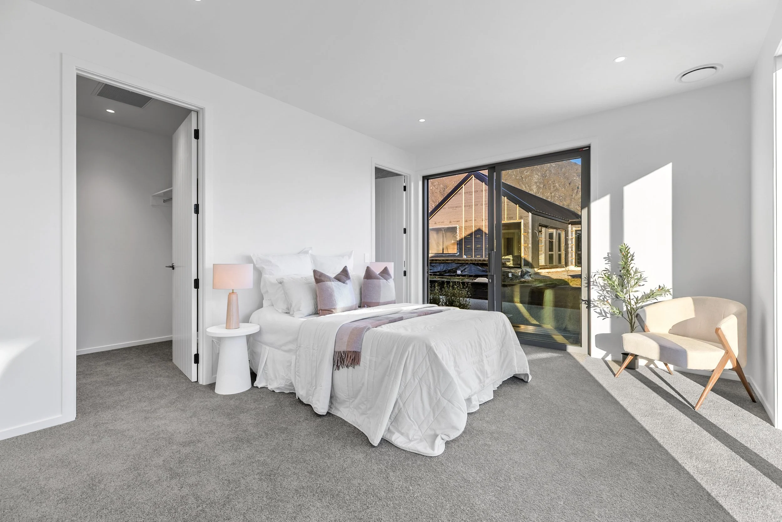 New build bedroom with white bedding, sliding glass doors, and hillside views — Jacks Point, Queenstown