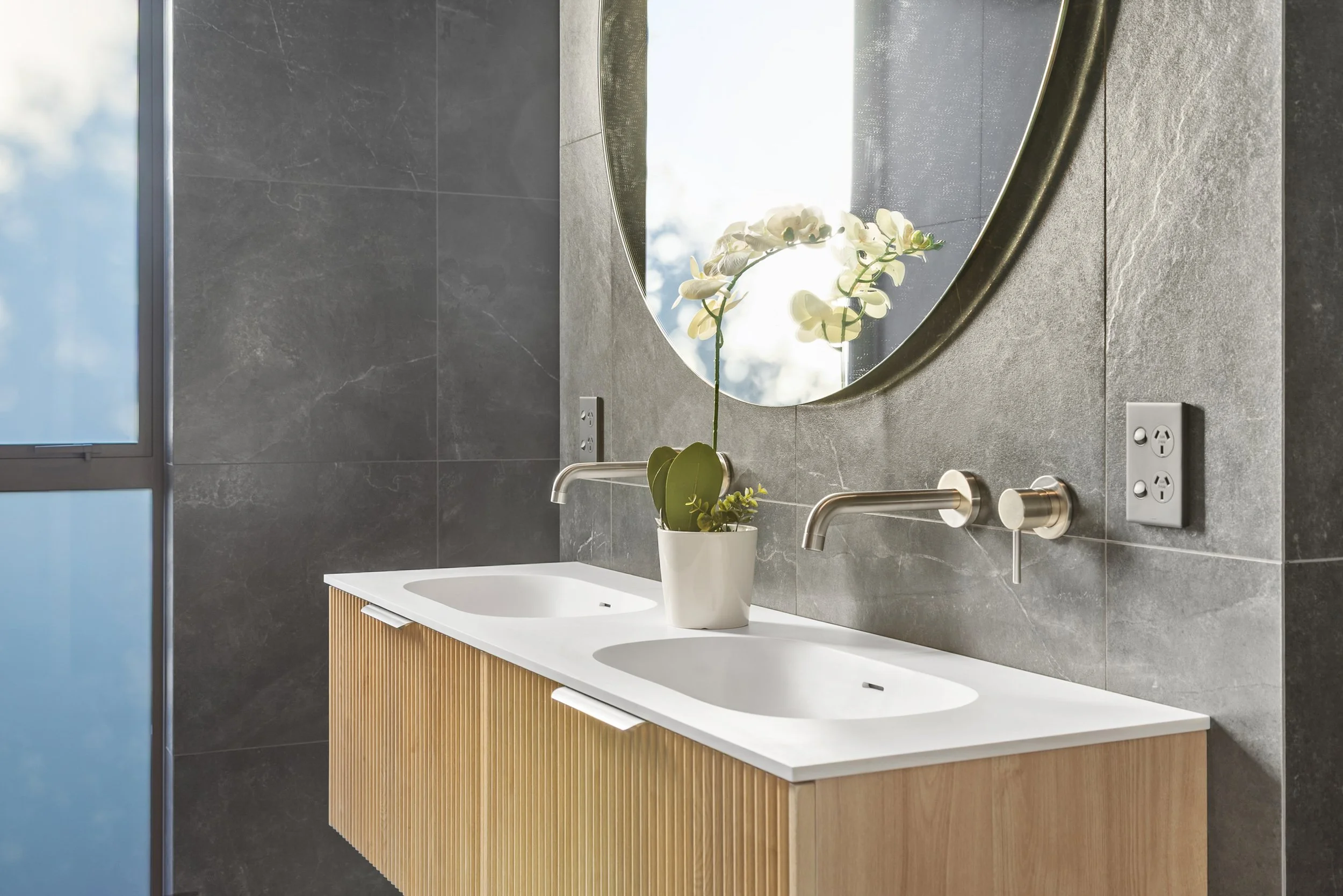 New build bathroom with grey tiles, round mirror, and orchid on wooden vanity — Jacks Point, Queenstown