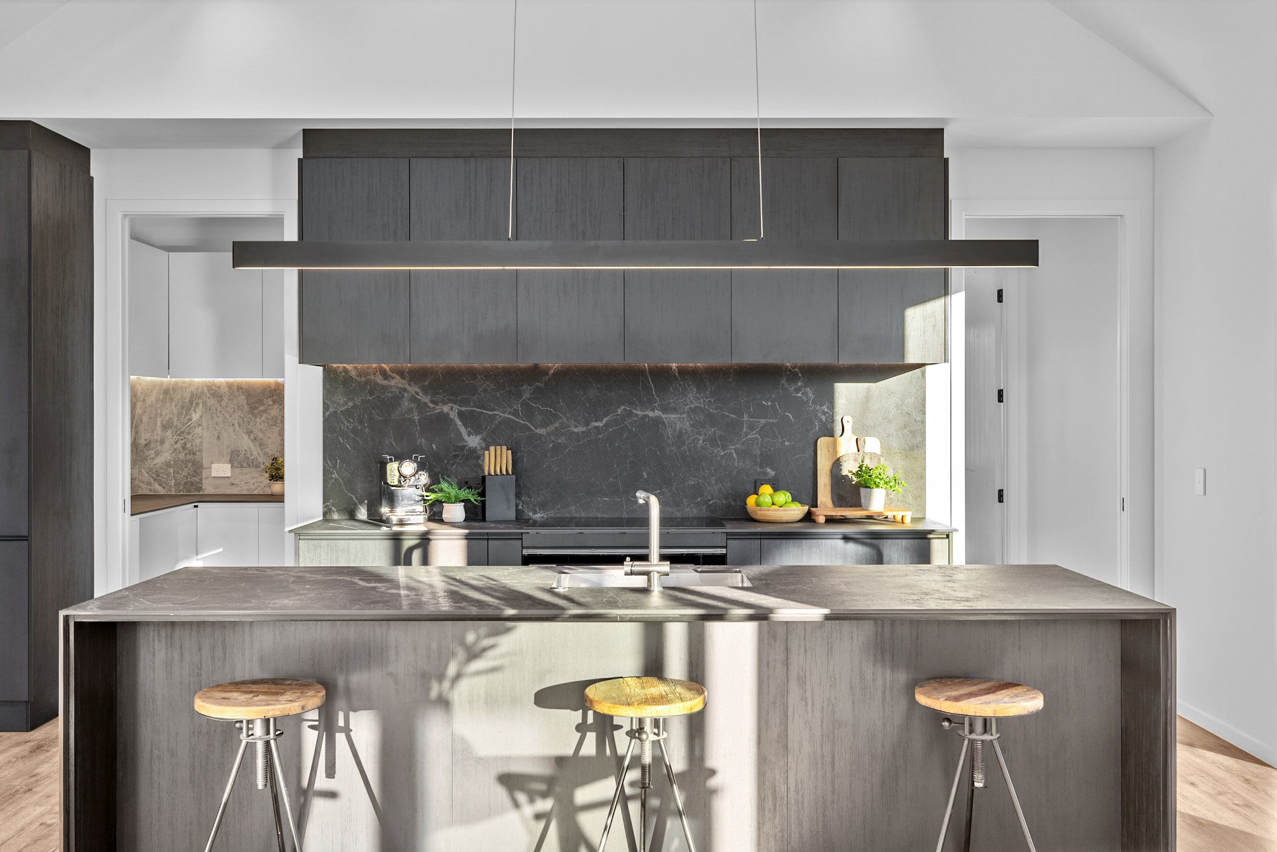 New build kitchen with grey cabinetry, marble backsplash, and wood and metal island stools — Jacks Point, Queenstown