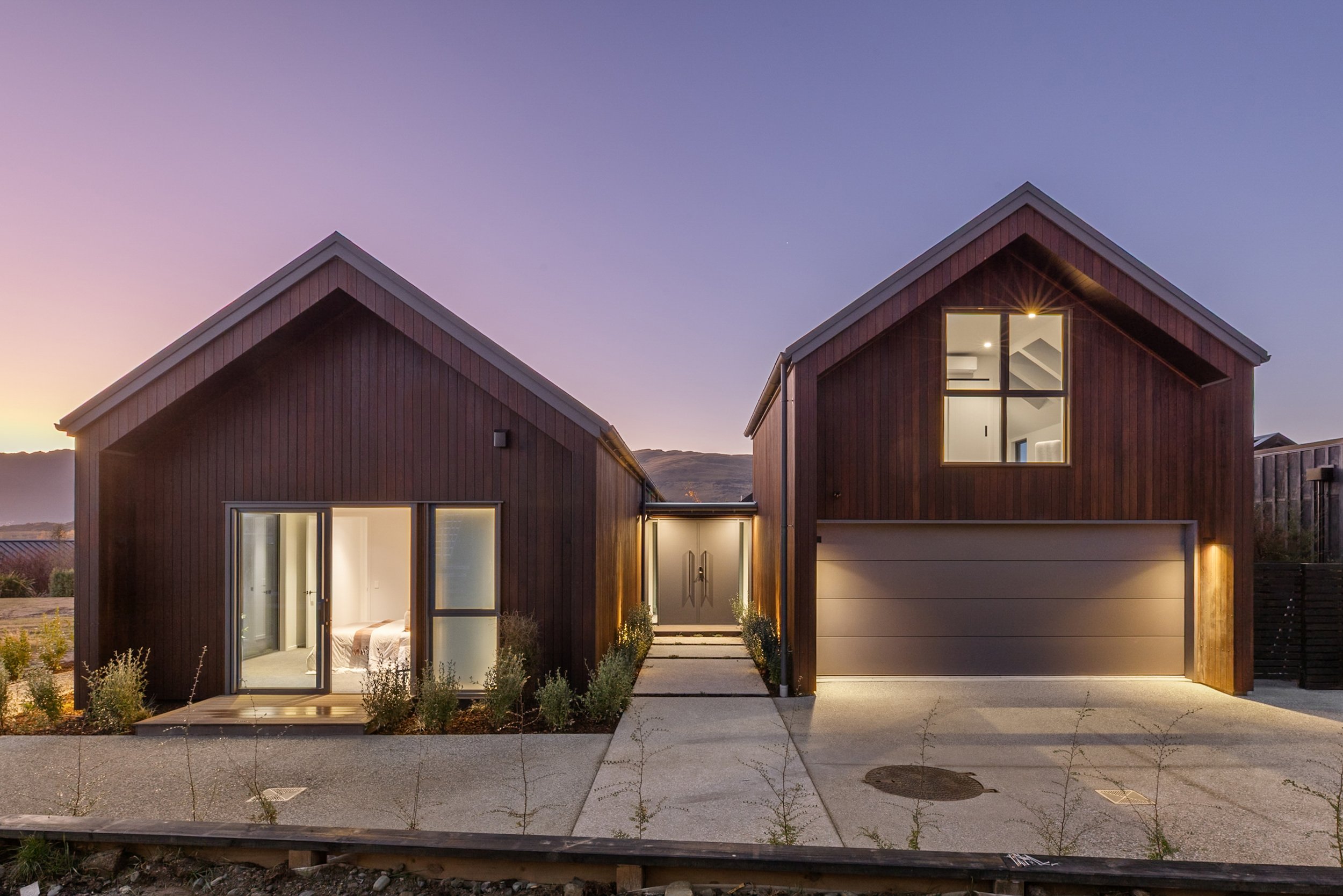 New build two-storey home exterior with wood siding, illuminated at dusk — Jacks Point, Queenstown
