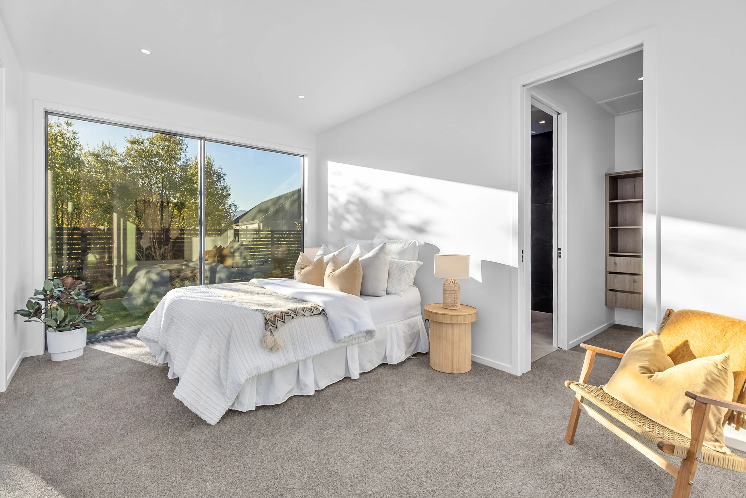 New build bedroom with tree-view window, woven lamp side table, and yellow accent chair — Jacks Point, Queenstown