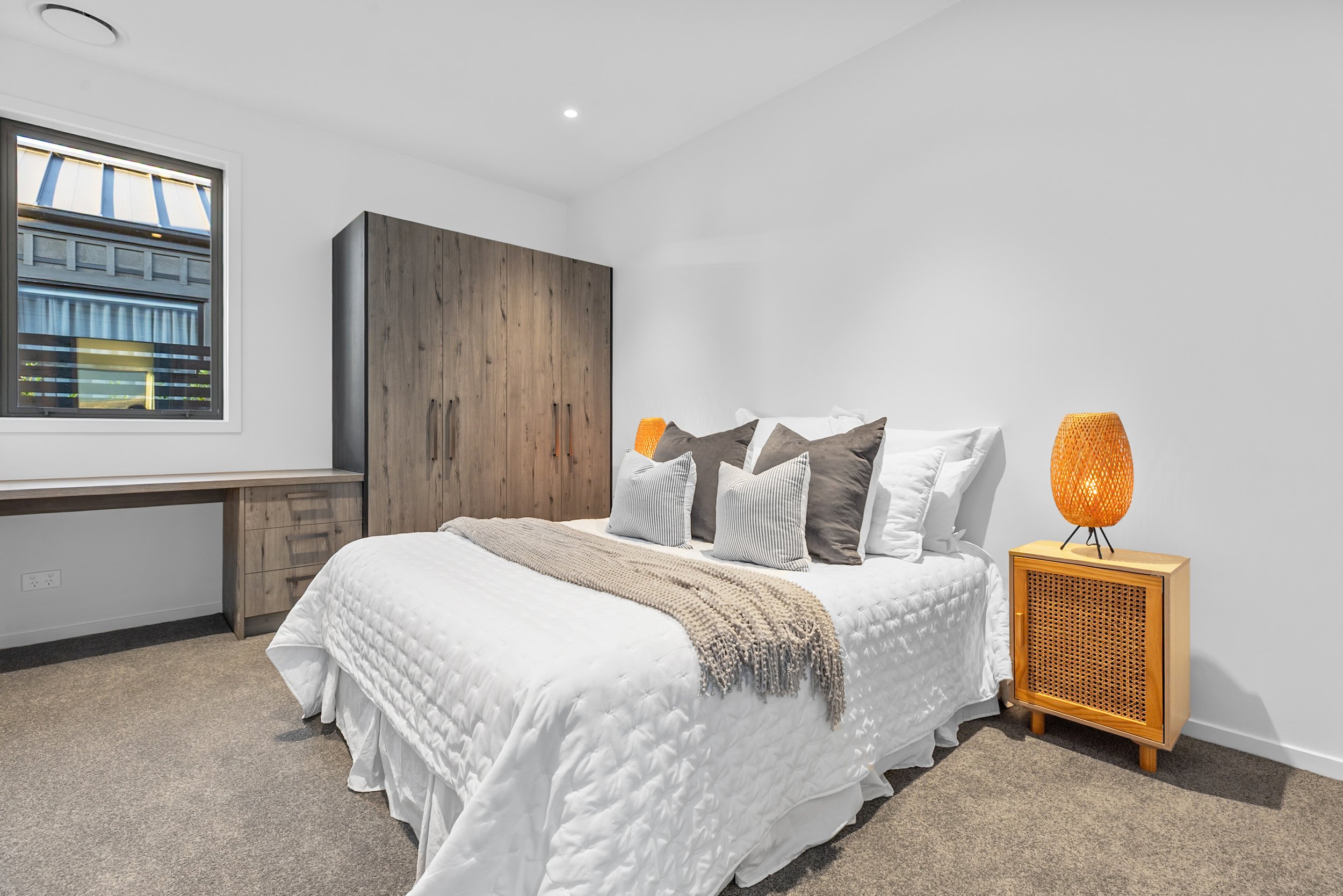 New build bedroom with white bedding, woven orange lamp, and wooden wardrobe — Jacks Point, Queenstown