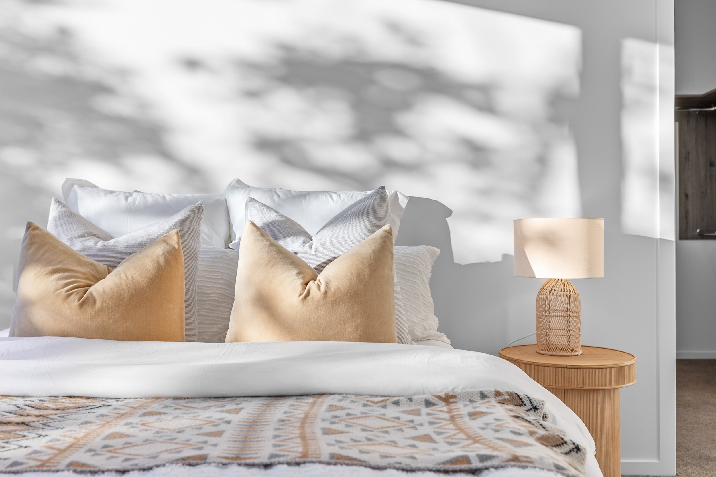 New build bedroom with layered beige, white, and grey pillows and wooden nightstand — Jacks Point, Queenstown