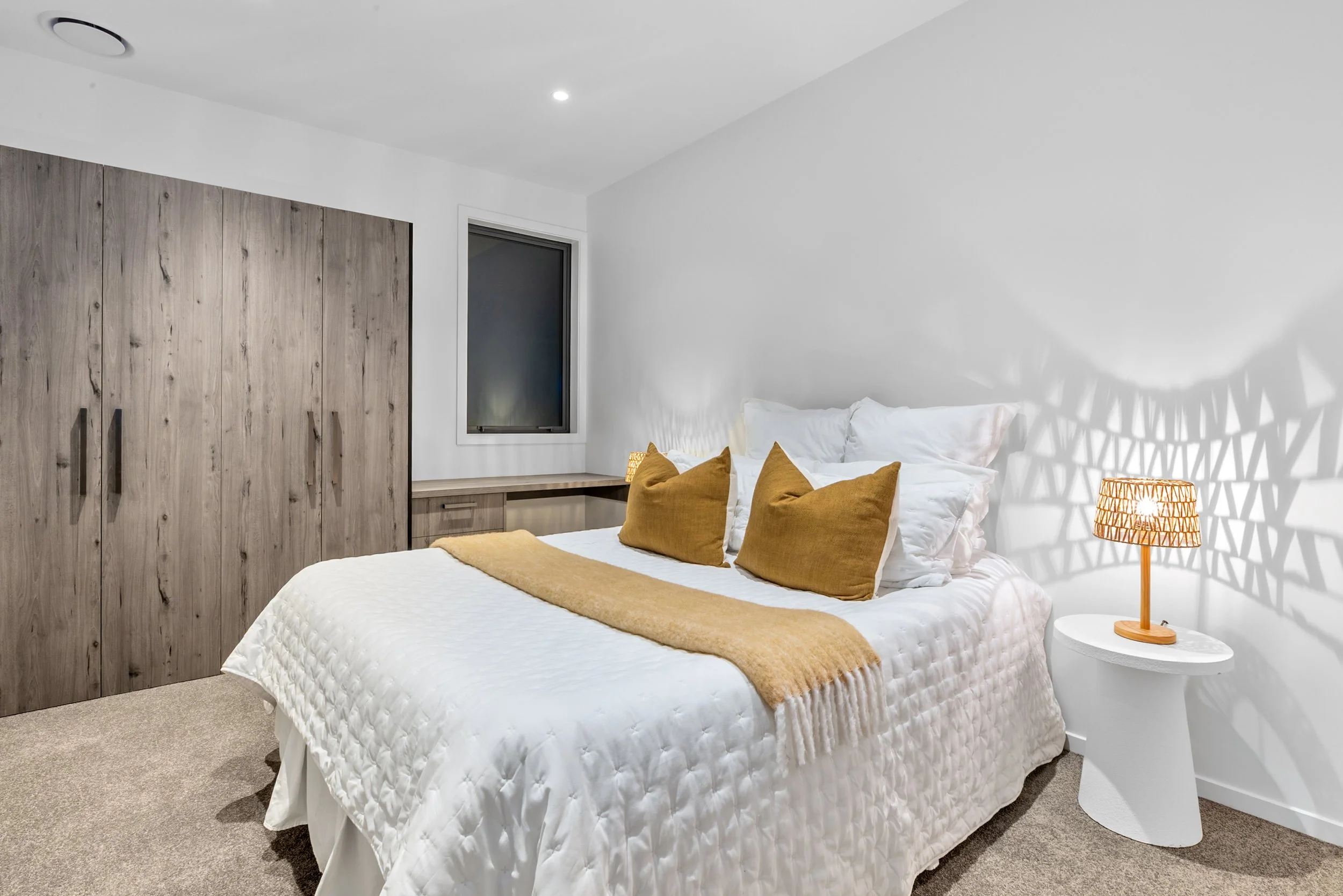 New build bedroom with white quilted bedspread, gold pillows, and wooden wardrobe — Jacks Point, Queenstown