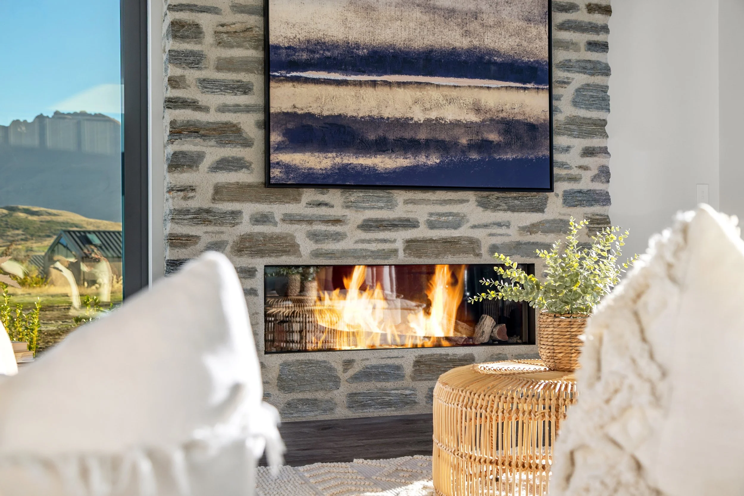 New build living room with stone fireplace, abstract artwork, and hillside views — Jacks Point, Queenstown