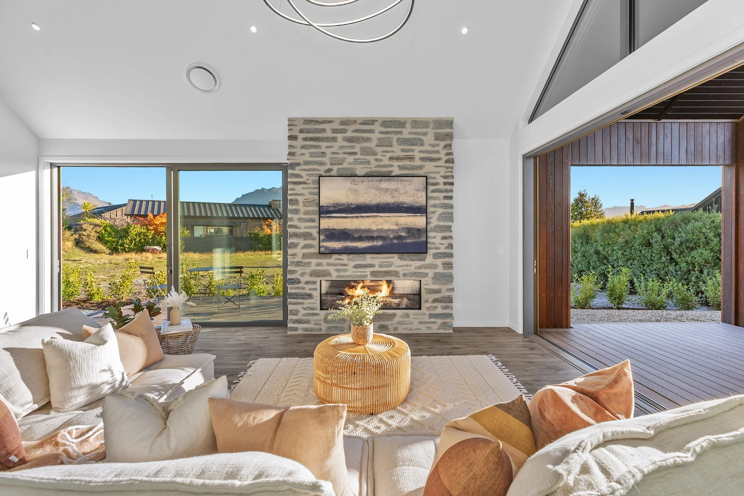 New build living room with stone fireplace, beige sofa, and sliding doors to garden and mountain views — Jacks Point, Queenstown