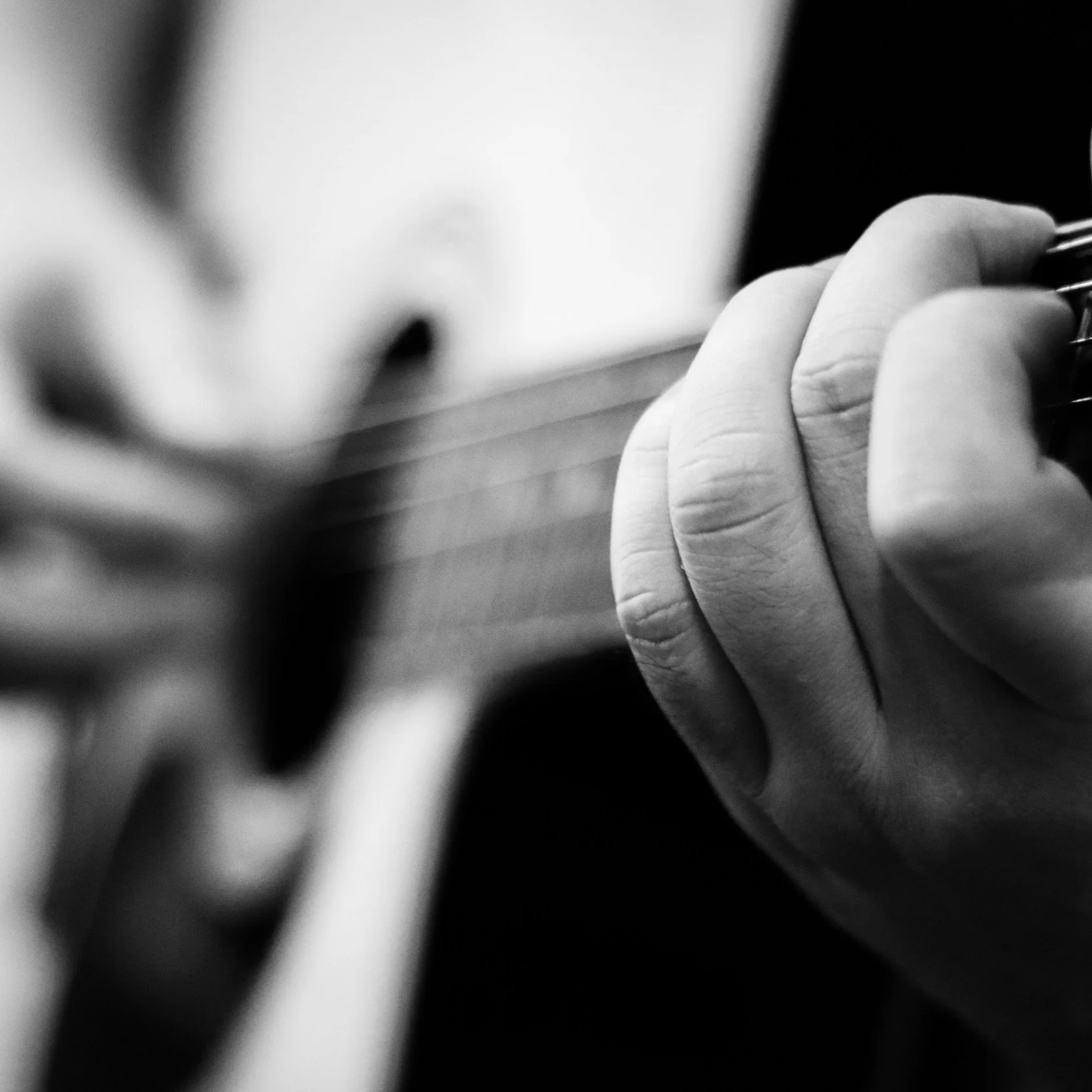 Close-up of a person's hand pressing strings on an acoustic guitar, black and white photo.