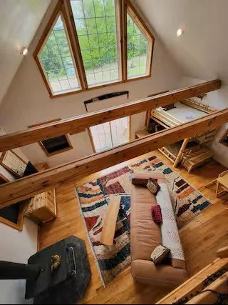 A cozy living room with a large window, a beige sofa with patterned pillows, a wooden coffee table, a colorful area rug, and wooden furniture.