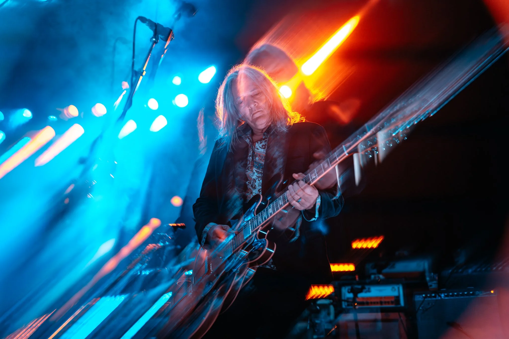 A musician playing an electric guitar on stage during a live performance with colorful stage lights creating a vibrant atmosphere.