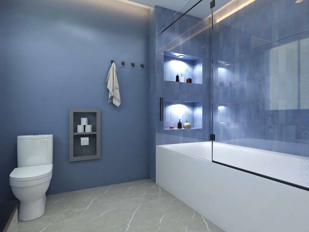 Modern bathroom with blue tiles, a white bathtub, a toilet, and built-in wall shelves with toiletries, illuminated by recessed lighting.
