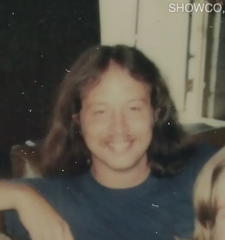 A person with long hair smiling in a casual setting, wearing a dark shirt.