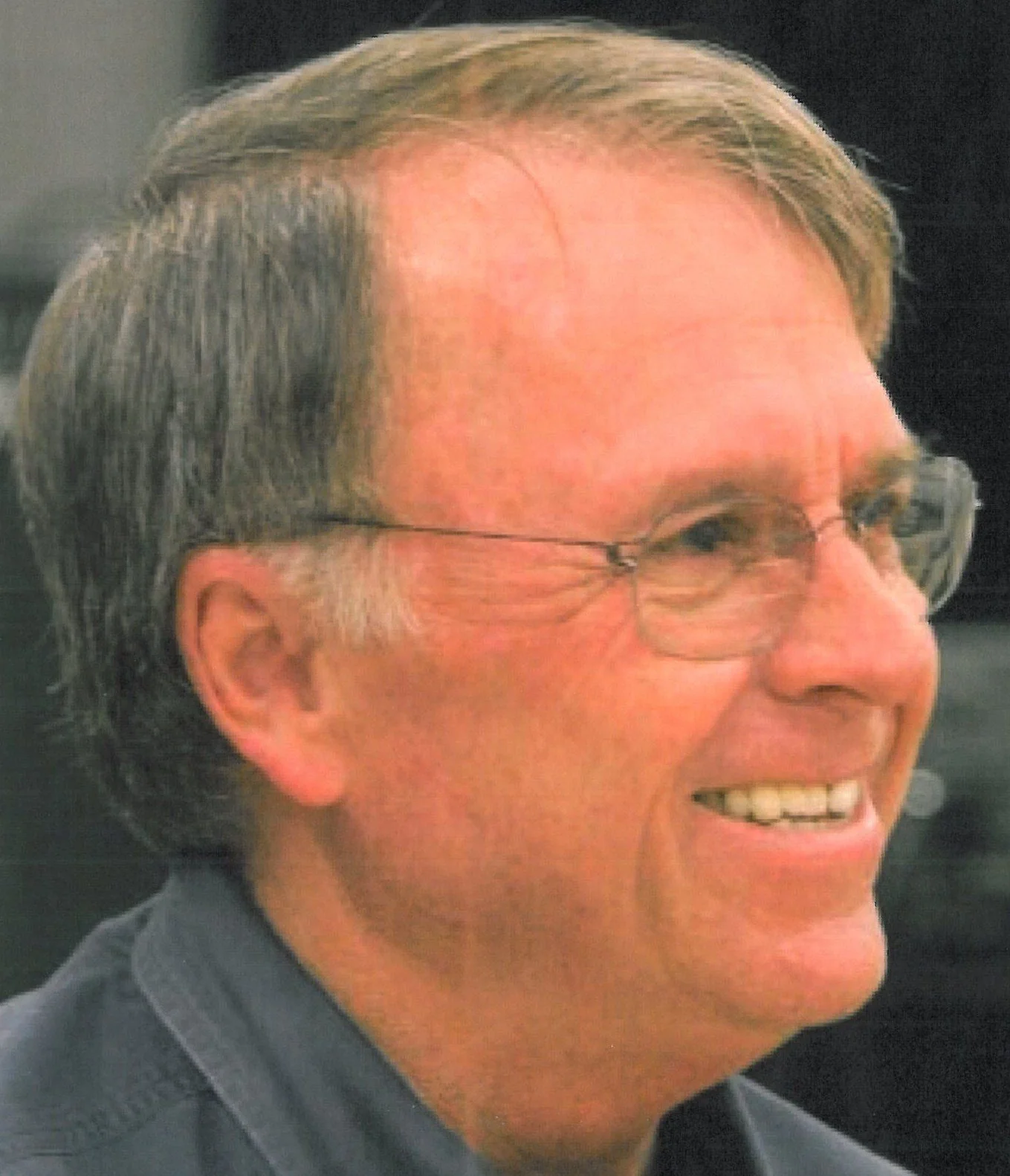 A middle-aged man with glasses and gray hair smiling, turned to the side.