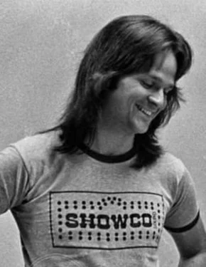 A woman with shoulder-length hair wearing a T-shirt that says 'SHOWCO' and smiling.