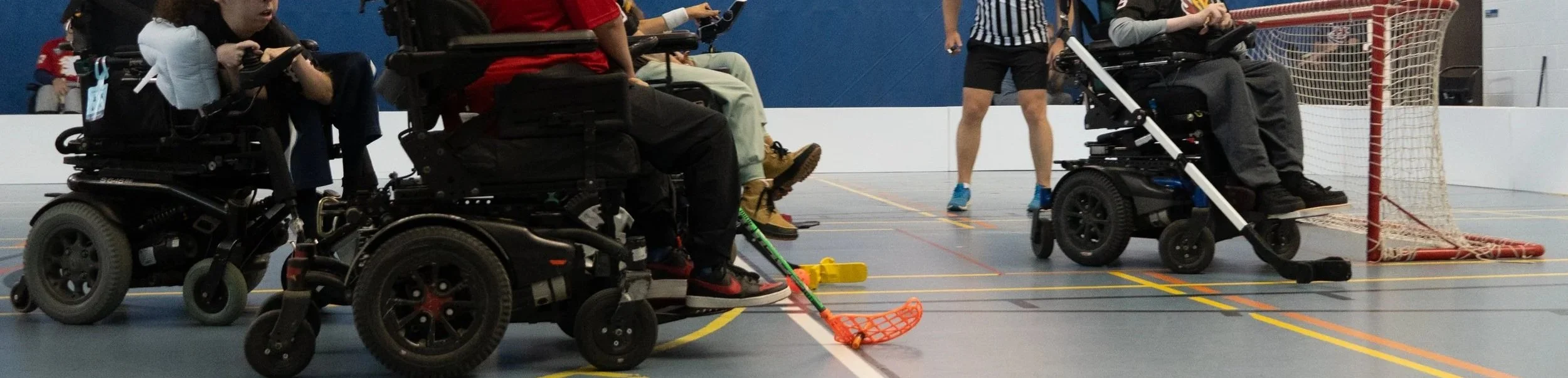 People in wheelchairs playing indoor hockey in a gymnasium.