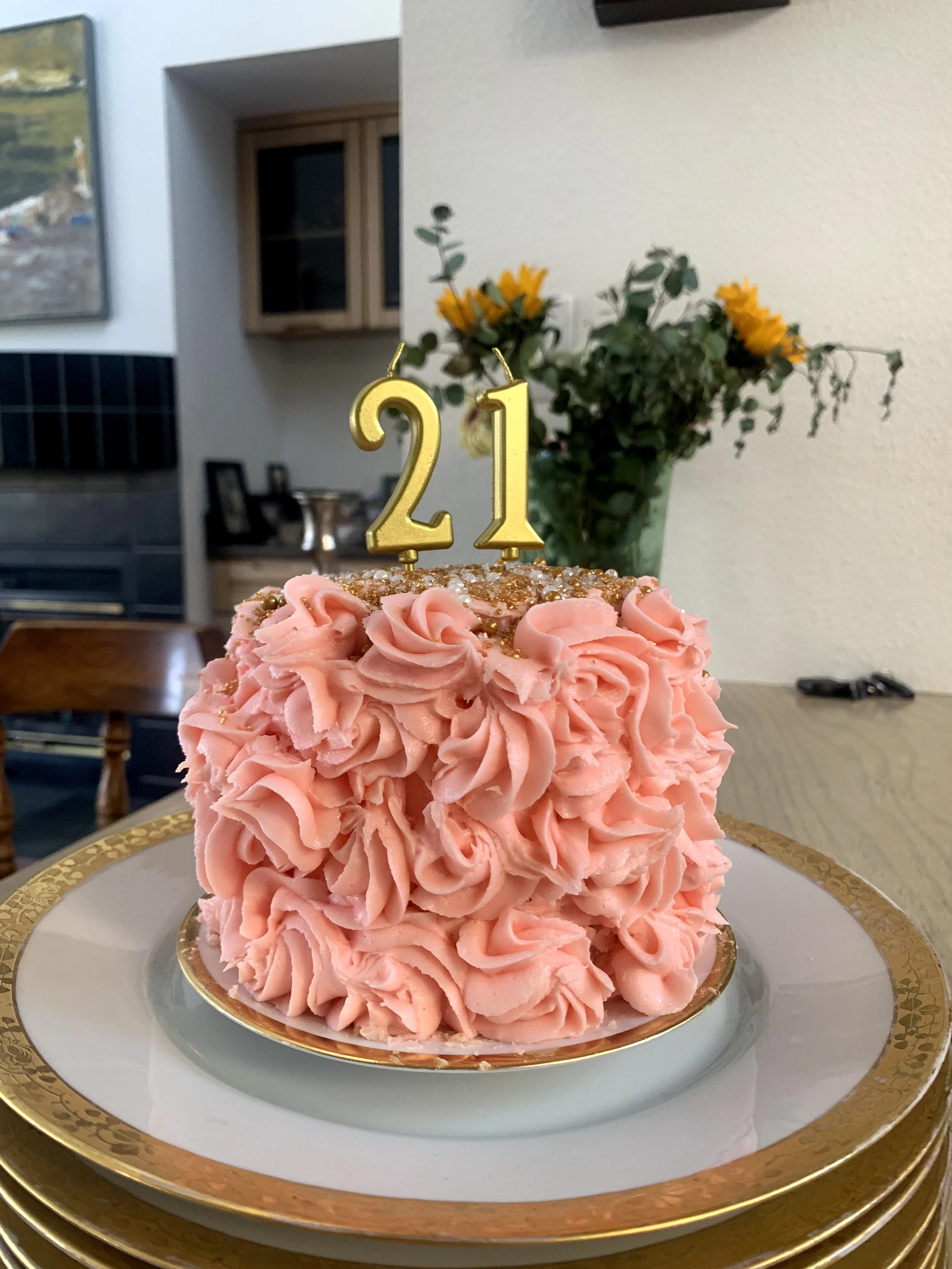 Pink ruffled cake with gold number 21 candle on top, placed on a white and gold plate.