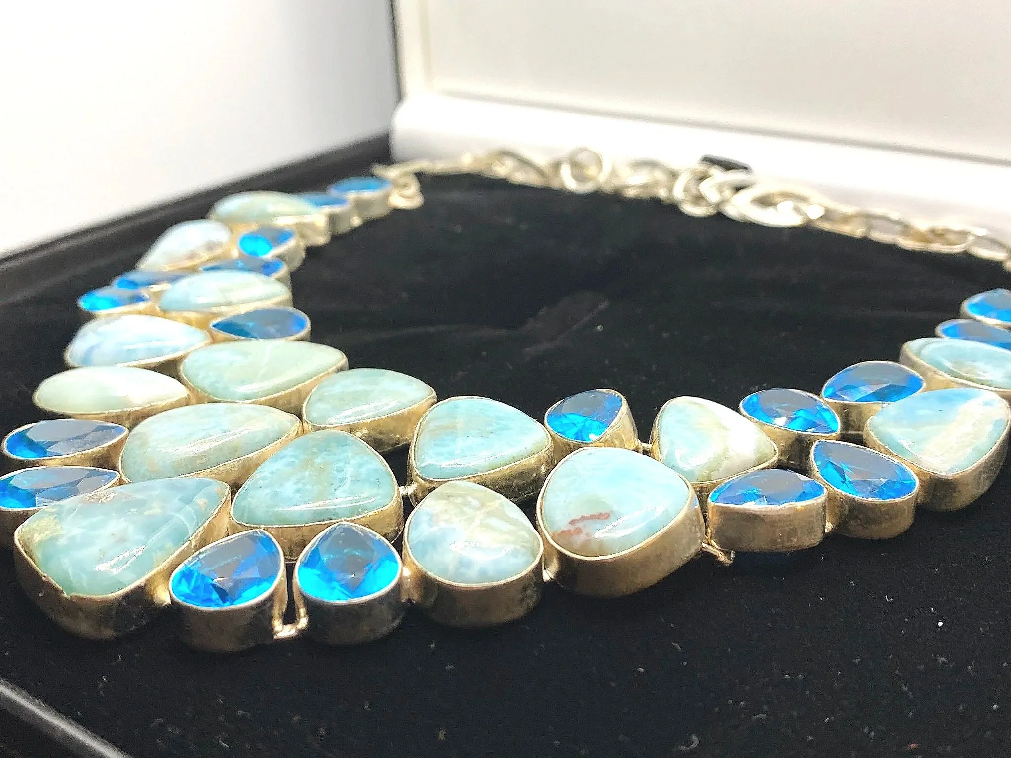 A larimar necklace with large blue topaz gemstones set in a silver chain displayed on a black velvet surface.