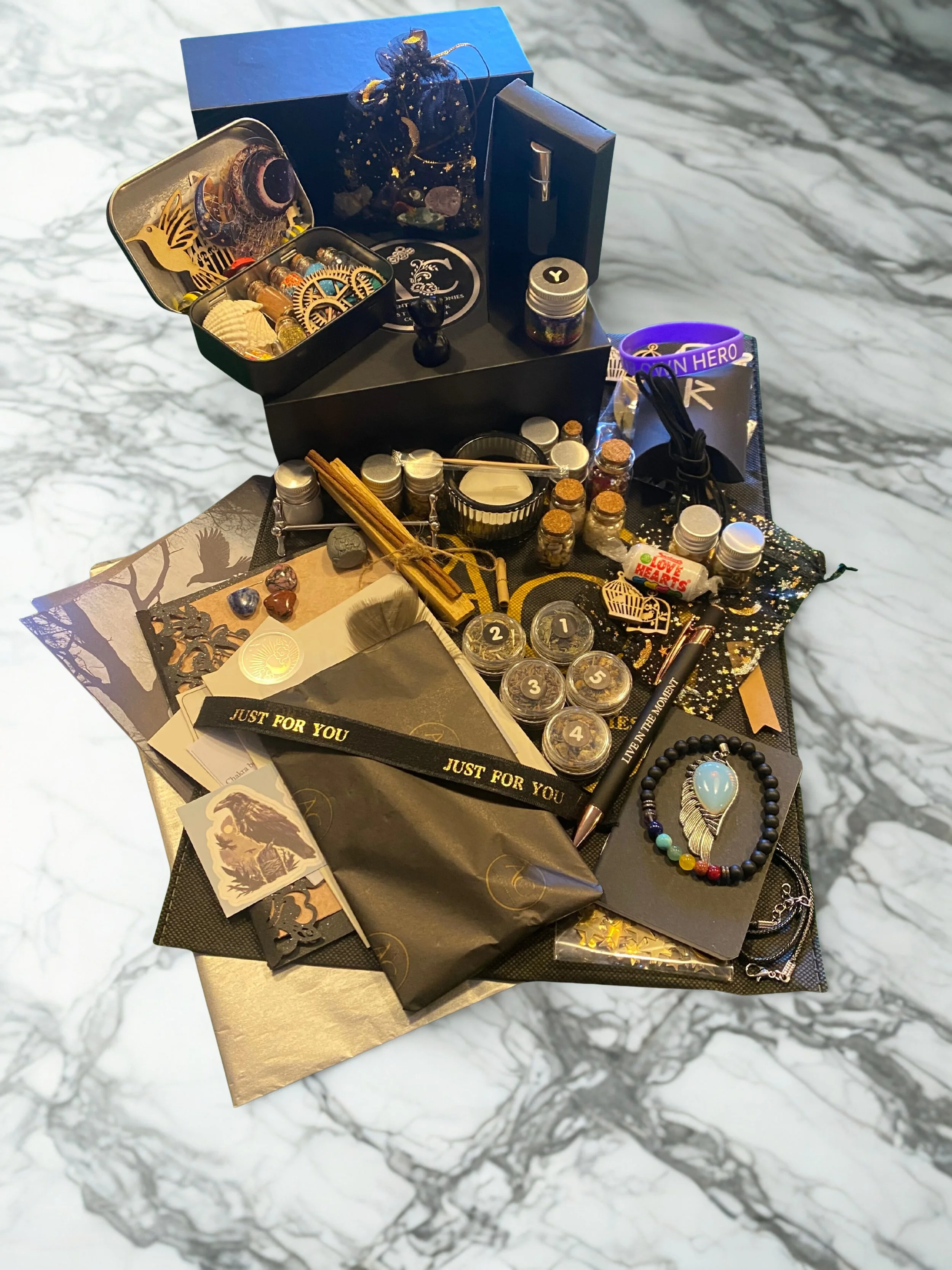 A collection of grief healing and spiritual items, including symbolic totems, essential oils, crystals, a mala bead bracelet, a wrapped gift box, incense, and craft items, arranged on a marble surface with a Authentic Ceremonies box.