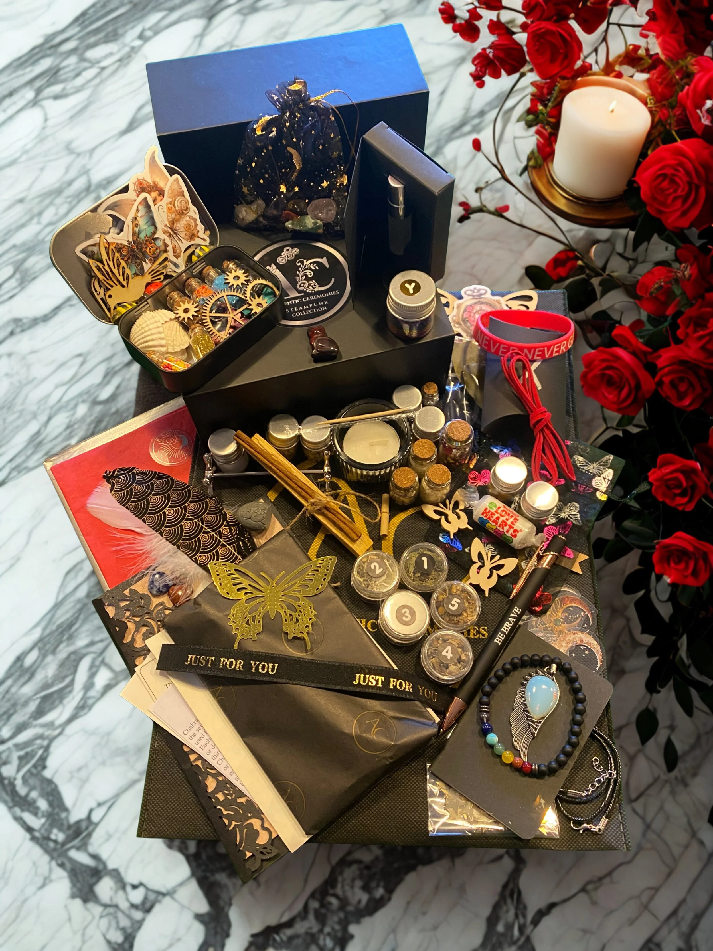 A collection of manifestation and spiritual items, including symbolic totems, essential oils, crystals, a mala bead bracelet, a wrapped gift box, incense, and craft items, arranged on a marble surface with an Authentic Ceremonies box.
