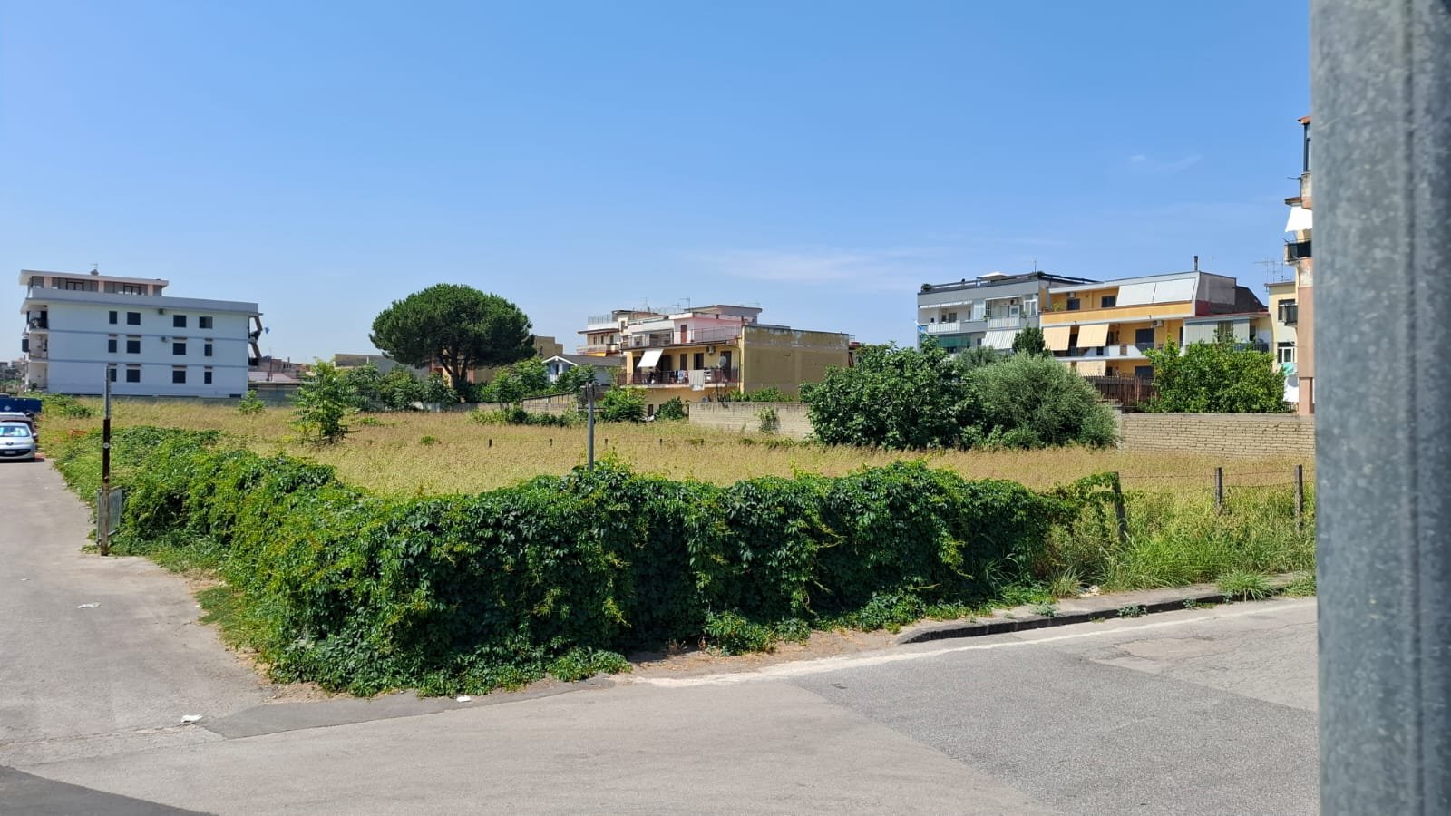 Vicinanza tra un prato verde e alcune case moderne su un colle, con cielo sereno.