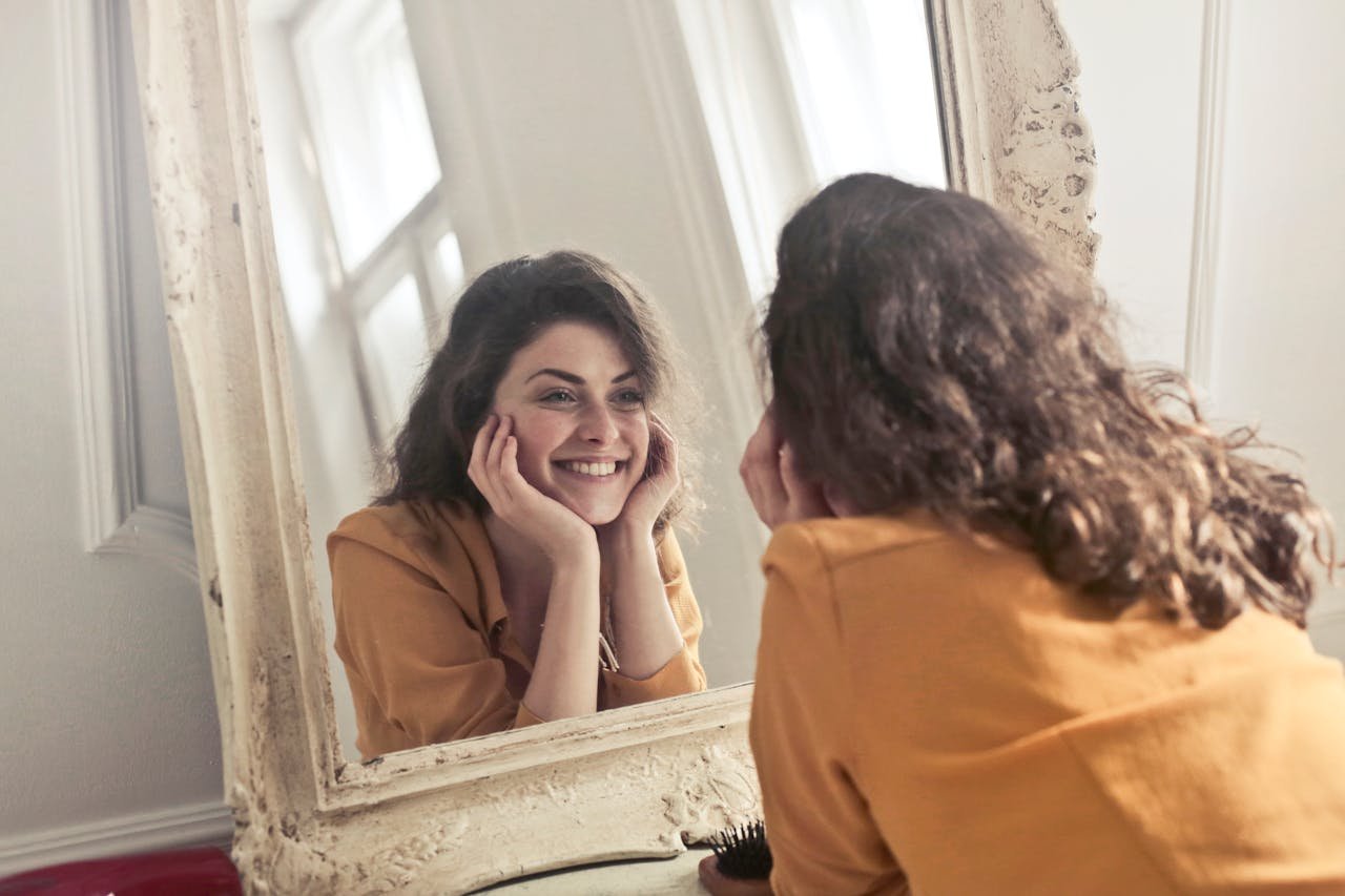 Woman looking at her reflection in a mirror with a contemplative expression; text overlay "Ekinetica Metamorphosis Intensive" and subtle landing-page call-to-action.